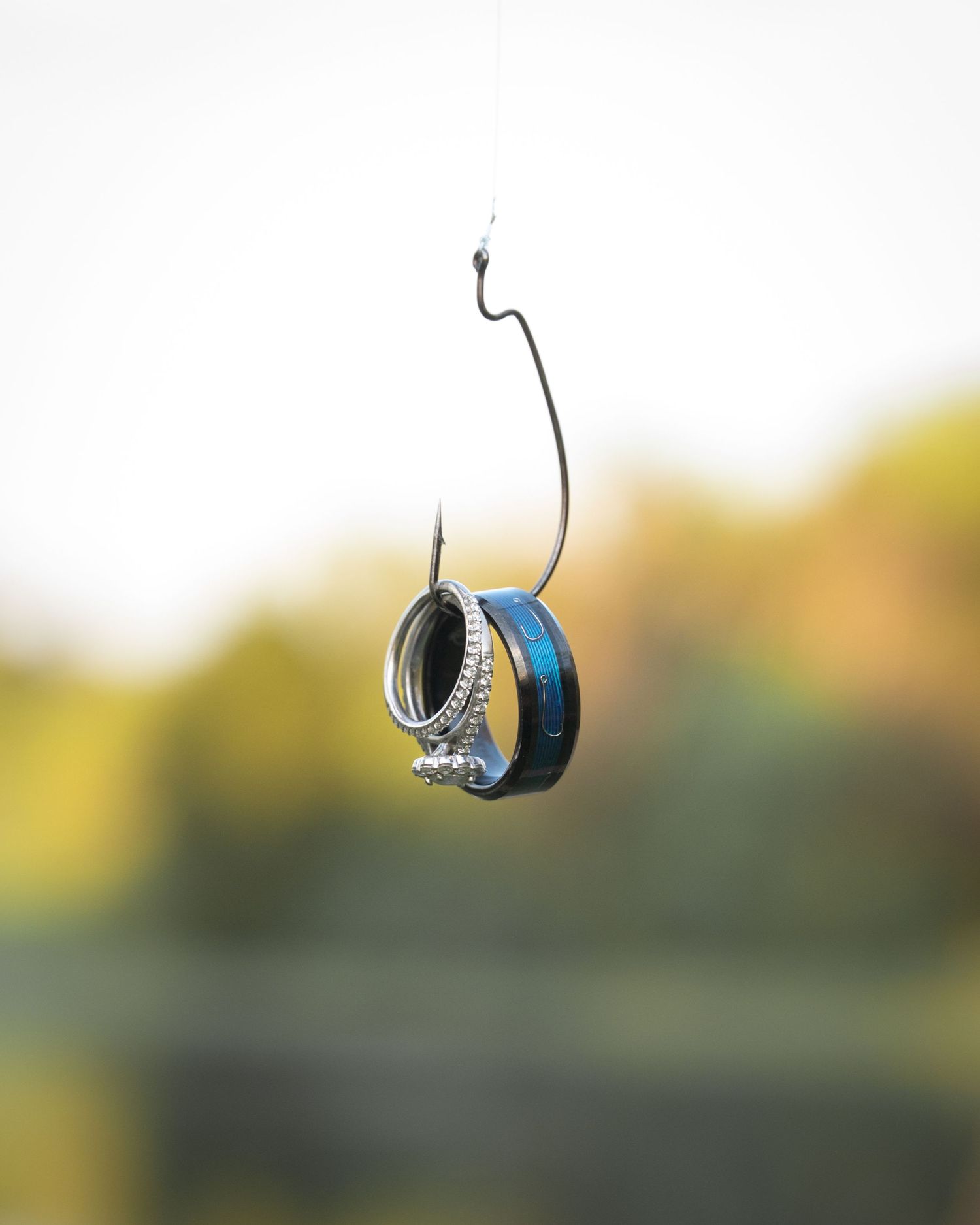Wedding rings elegantly displayed on a fishing hook with blurred outdoor background.