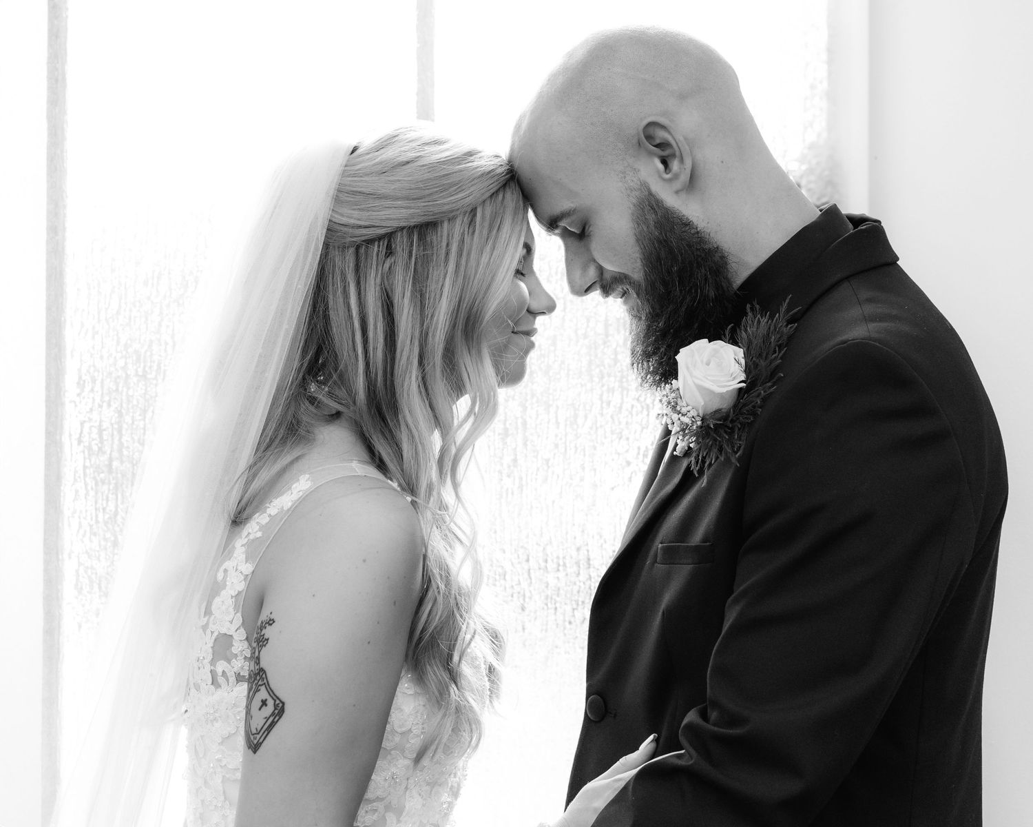 Black and white romantic photo of bride and groom touching foreheads tenderly on their wedding day.