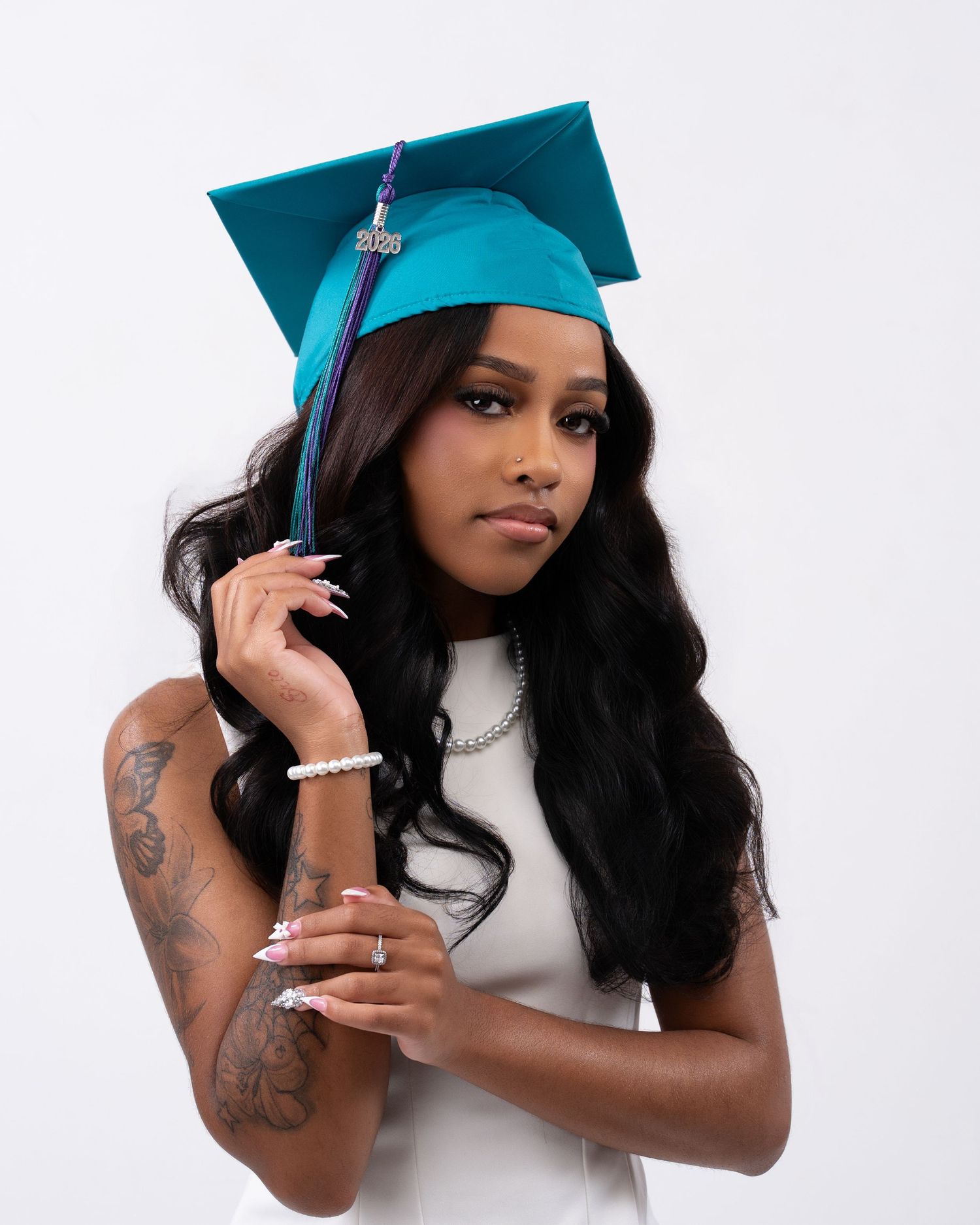 Young woman in teal graduation cap and white dress posing confidently for senior portrait.