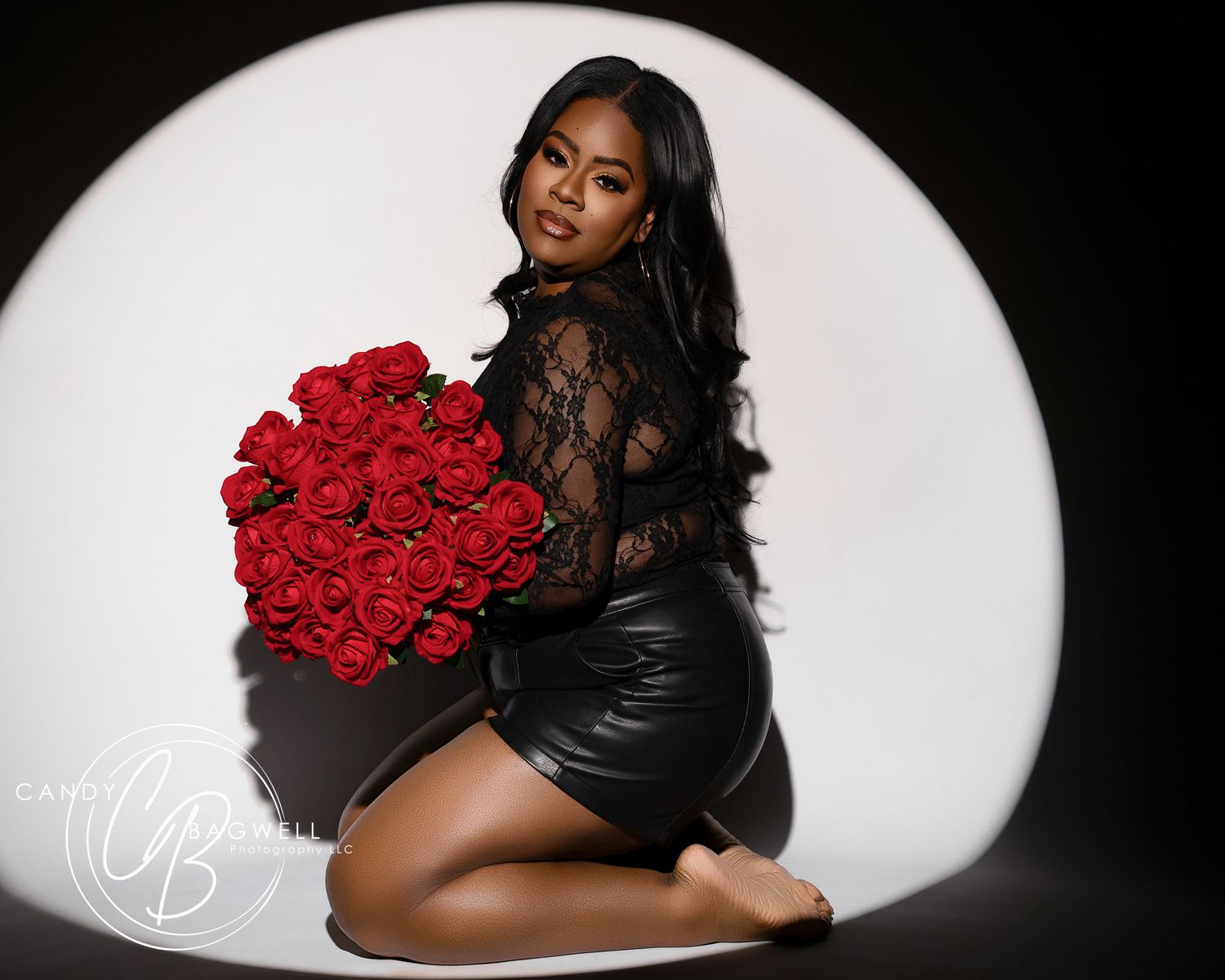 Woman in black lace top holds large bouquet of red roses in studio.