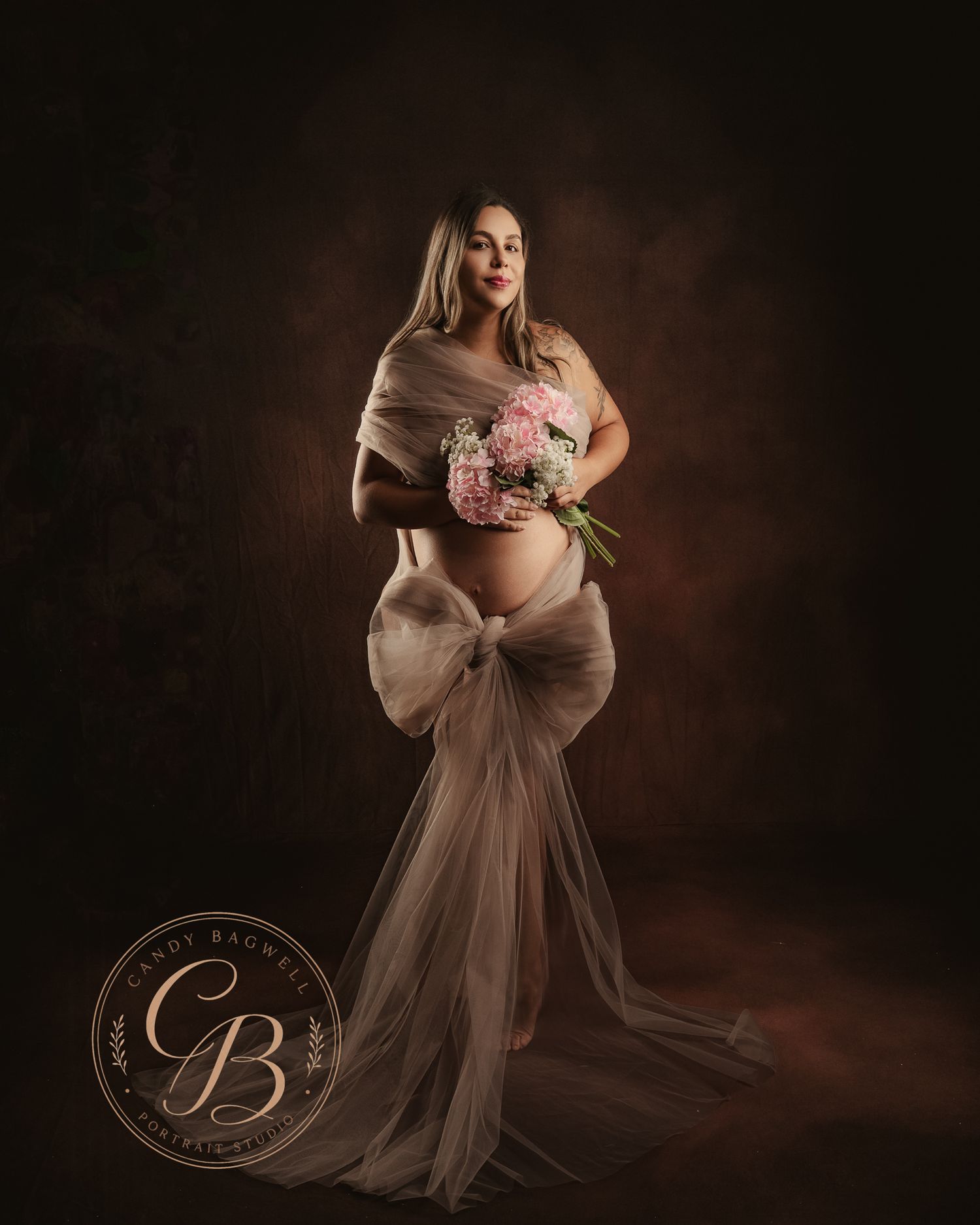 Pregnant woman in sheer blush gown holding pink floral bouquet, elegant maternity portrait by Cindy Bagwell Photography.