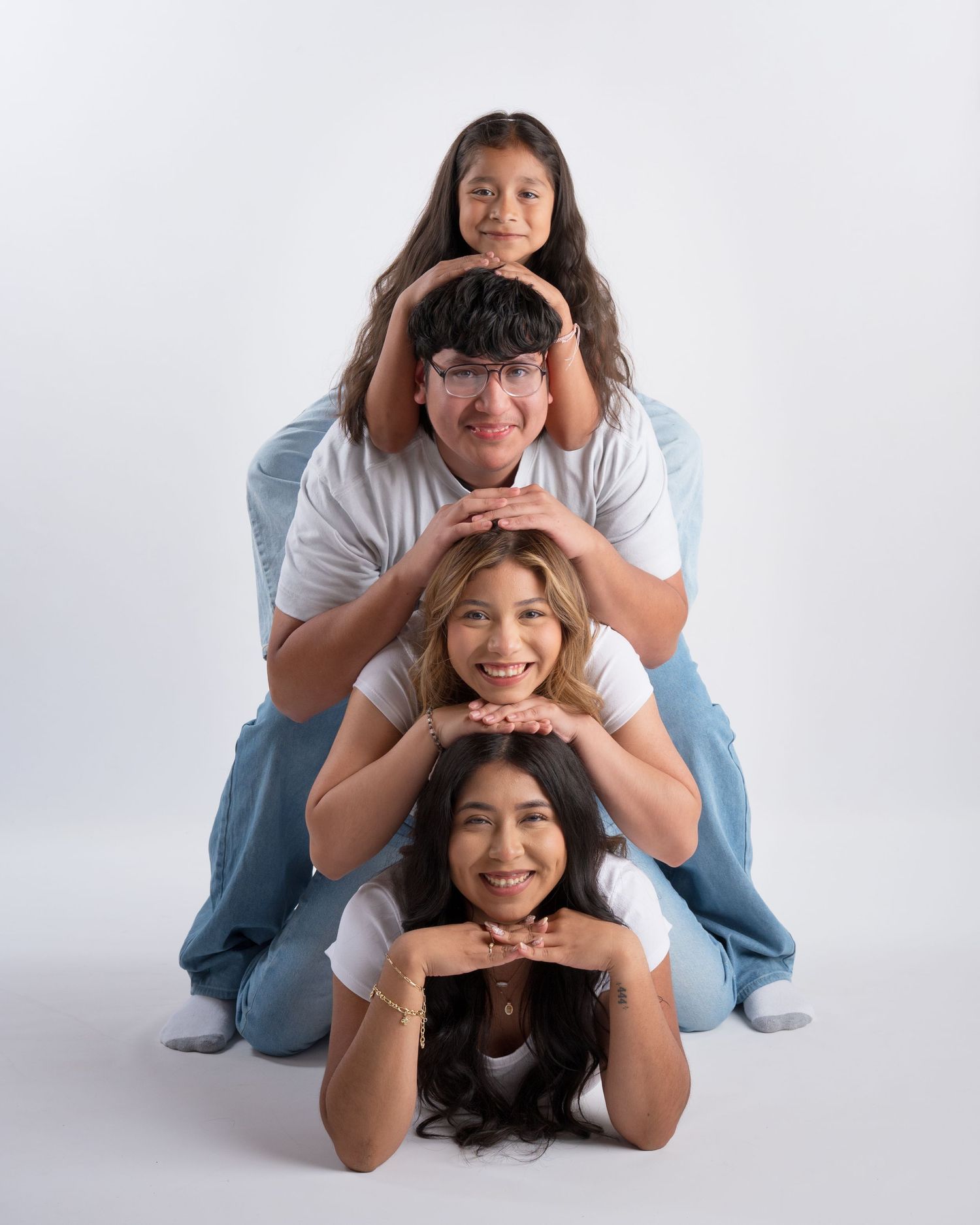Four siblings in white and denim outfits pose in a playful stacked formation in a studio.