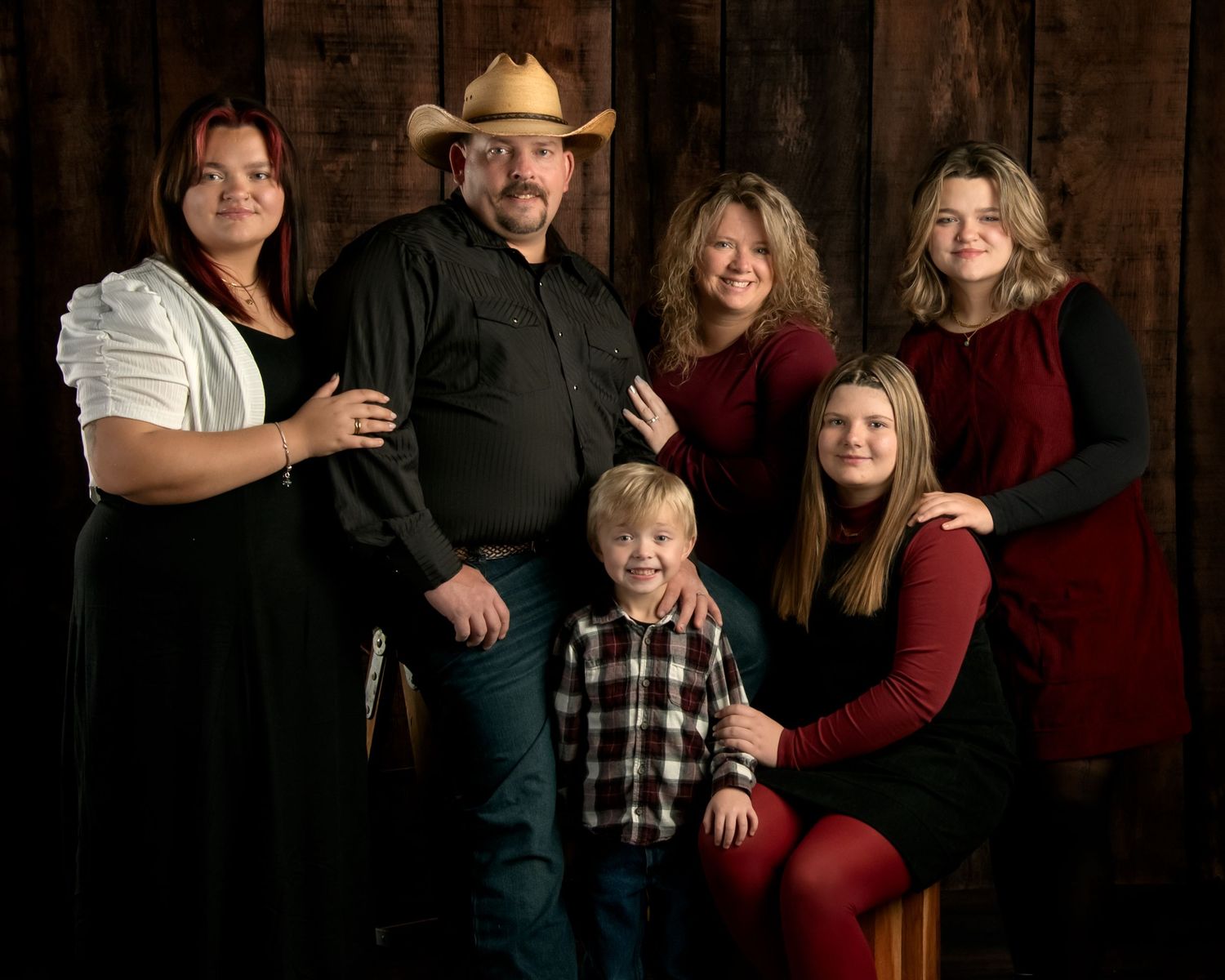 Family of six including parents and four children pose for portrait against rustic wood backdrop.