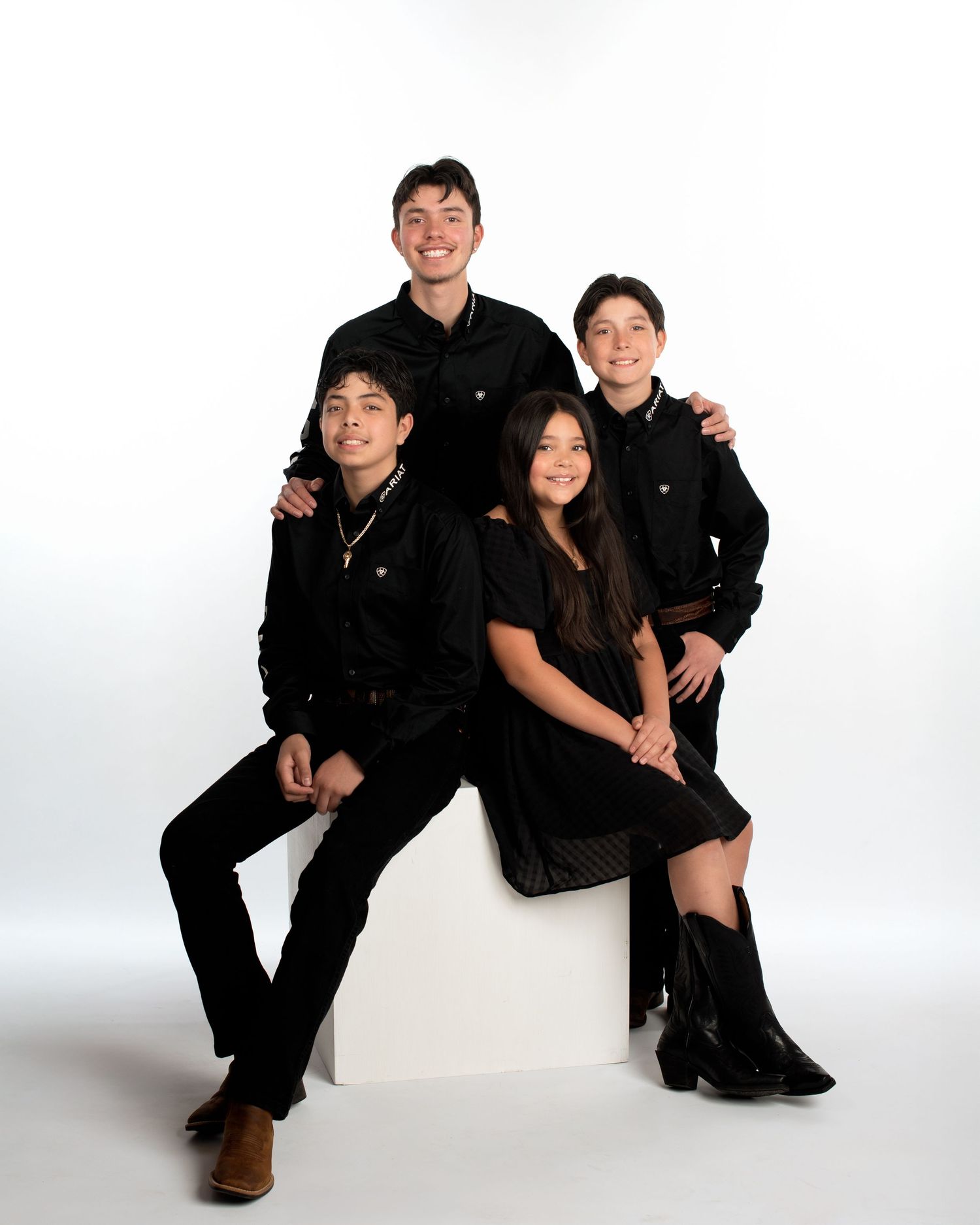 Four siblings in coordinated black outfits pose together in a professional family studio portrait.