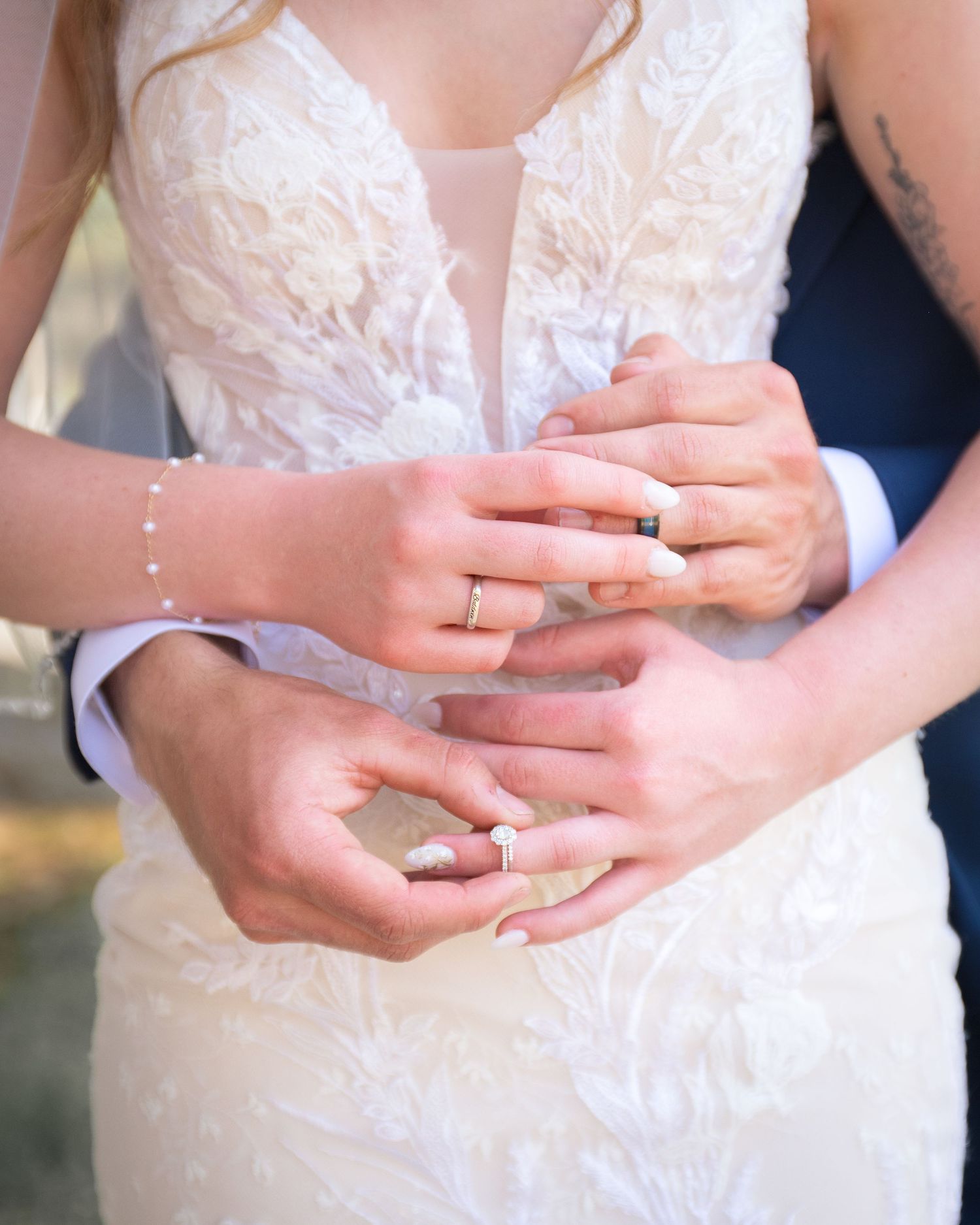 Close-up of bride and groom displaying wedding rings together against a lace bridal gown.