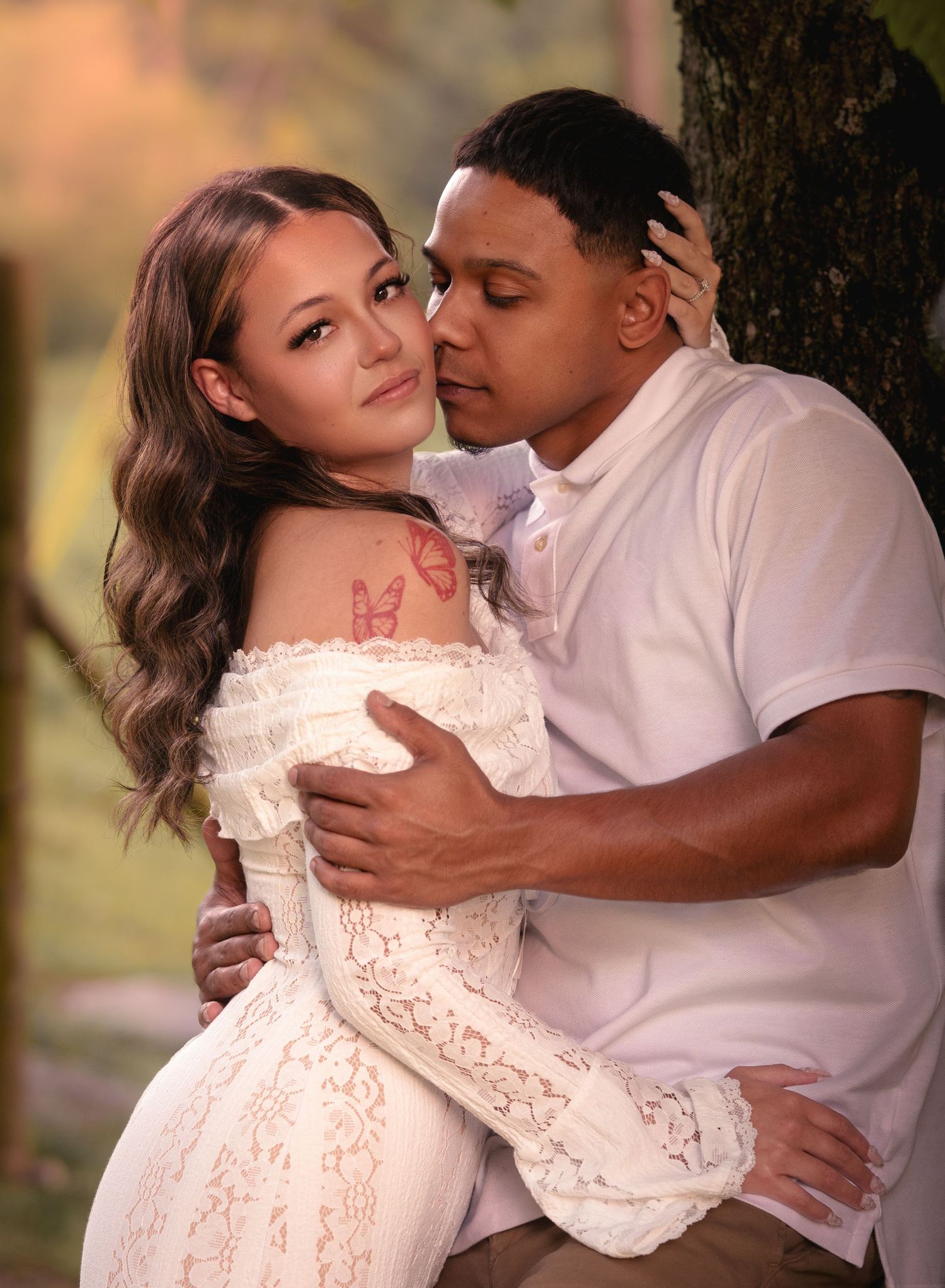 Romantic couple embracing near tree in warm golden outdoor light.