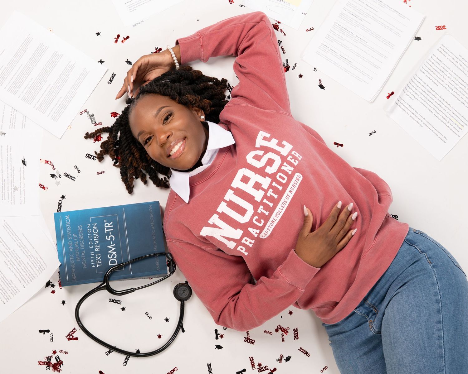 Nurse practitioner student lying among confetti with stethoscope and medical textbook.