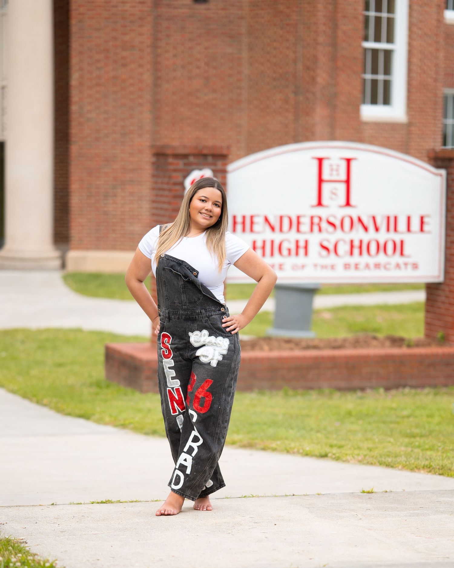 Young woman in painted graduation pants posing in front of Hendersonville High School sign.