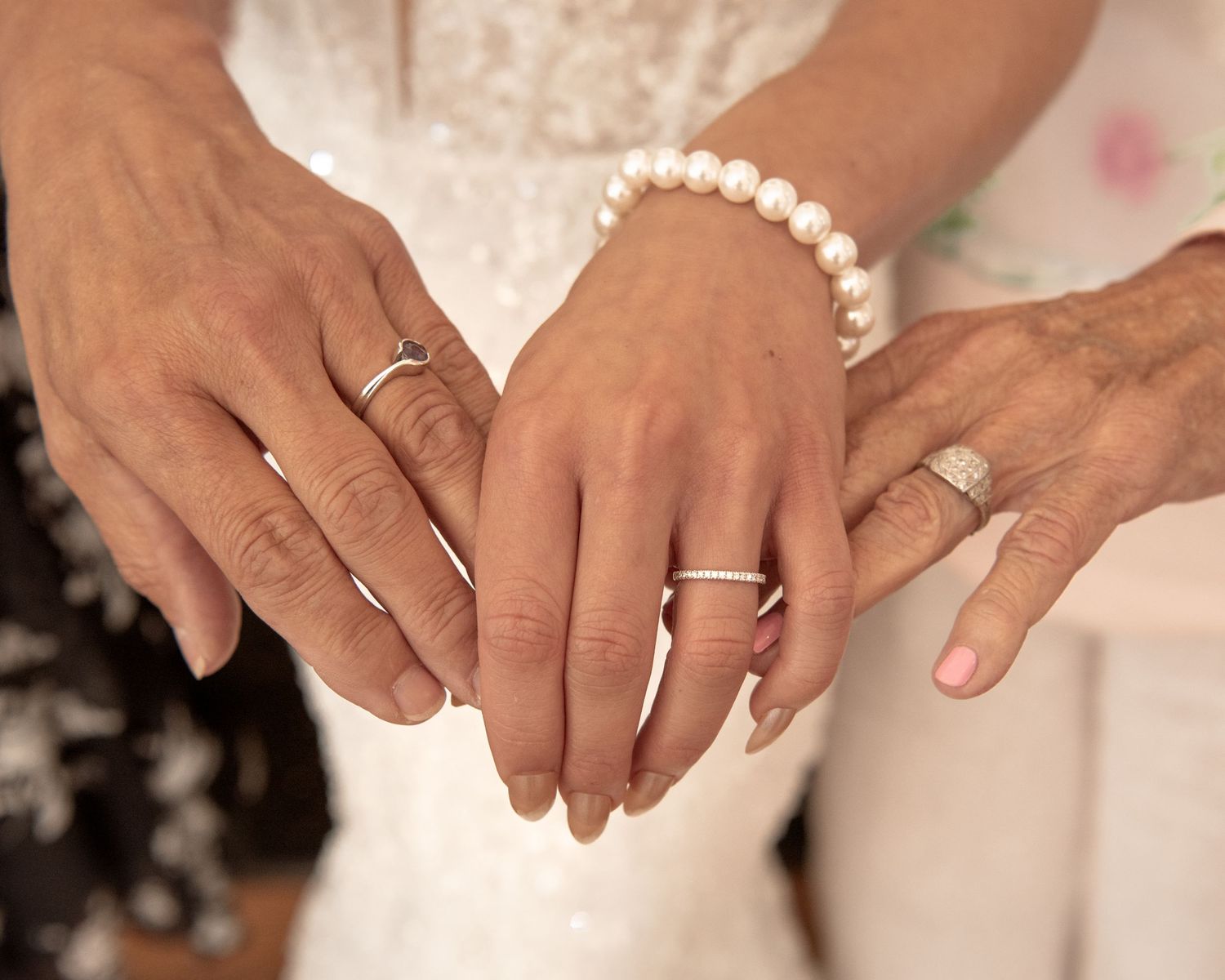 Three hands displaying wedding rings, bride wearing pearl bracelet in elegant ceremony moment.