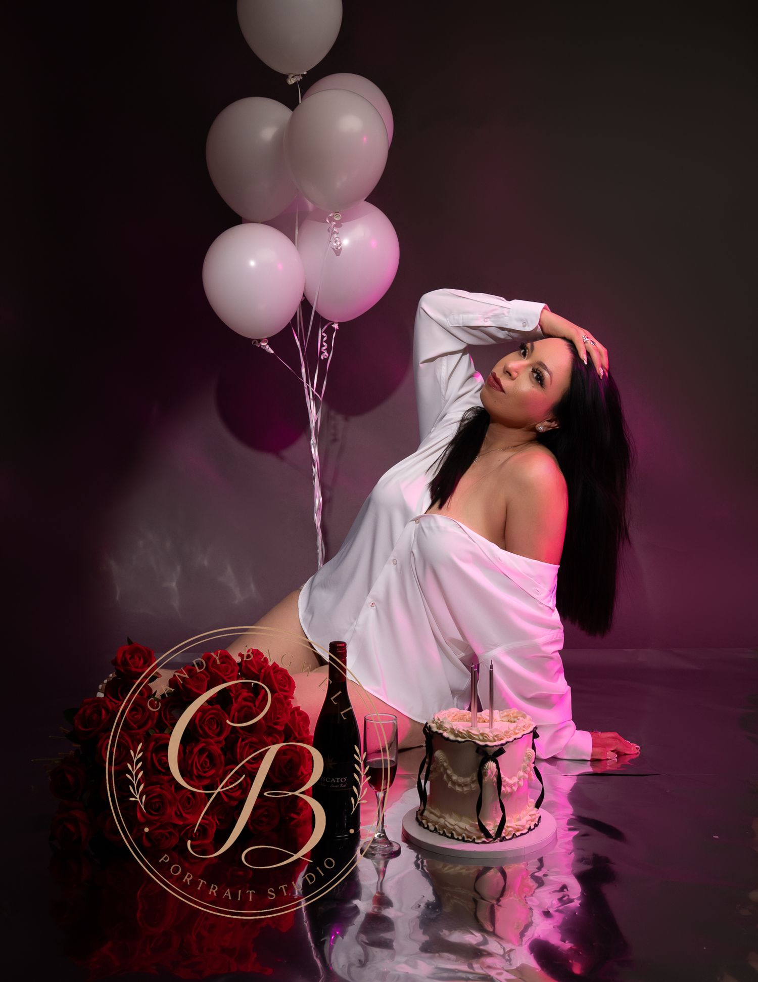 Woman in white shirt poses with pink balloons and birthday cake in studio.