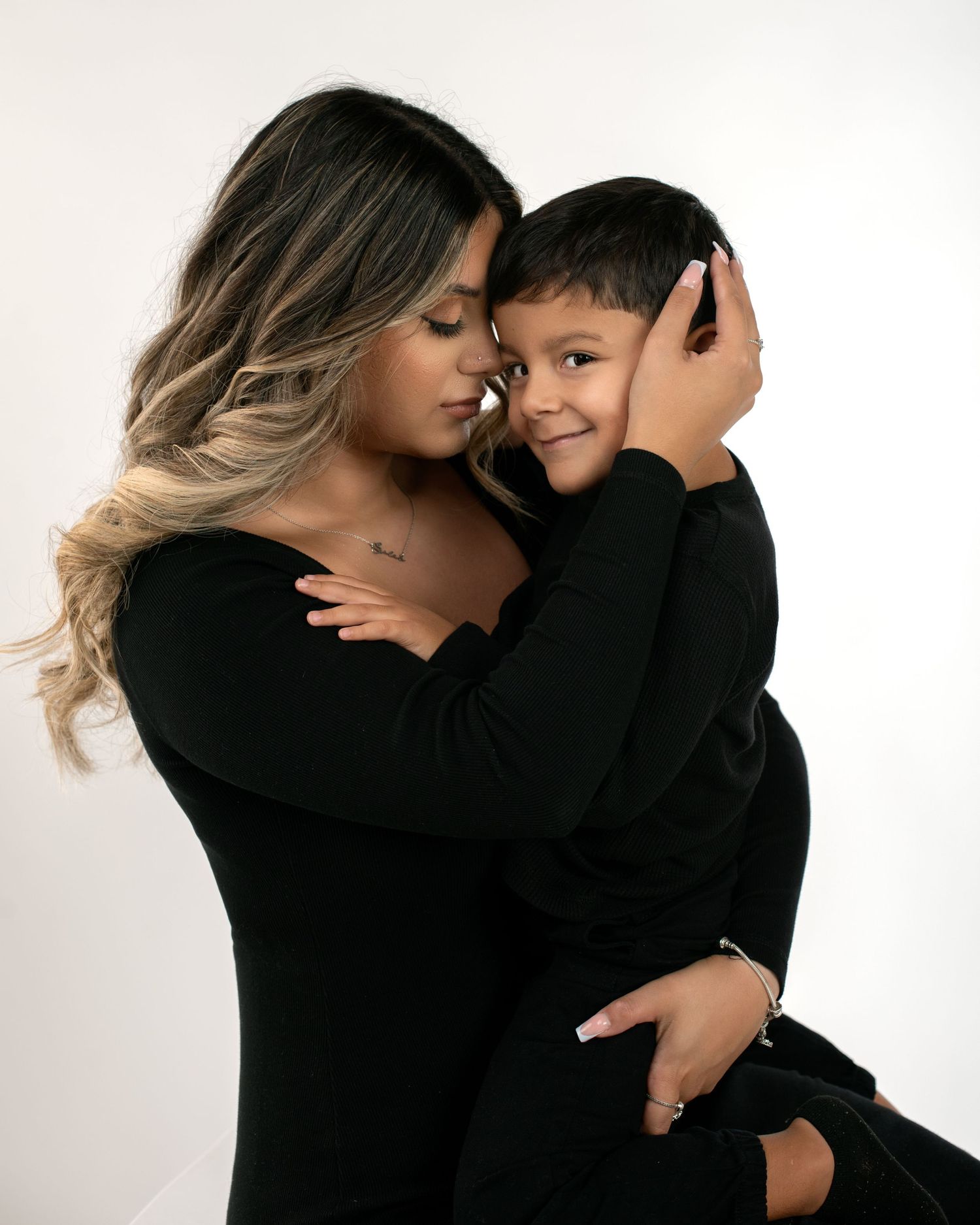 Loving mother in black dress tenderly embracing her young son in a white studio portrait.