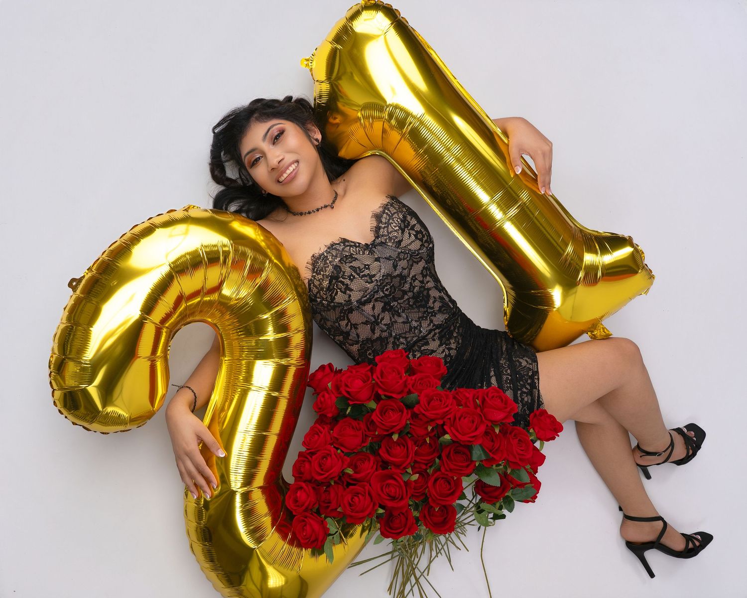 Woman celebrating 21st birthday with gold number balloons and red roses bouquet on white background.