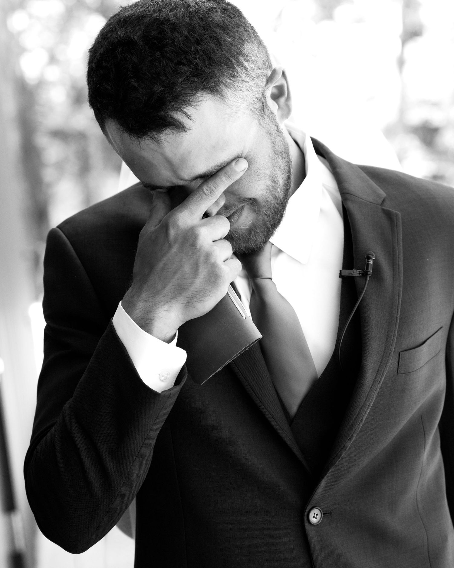 Emotional groom in black suit pinches his nose fighting back tears on his wedding day in black and white.