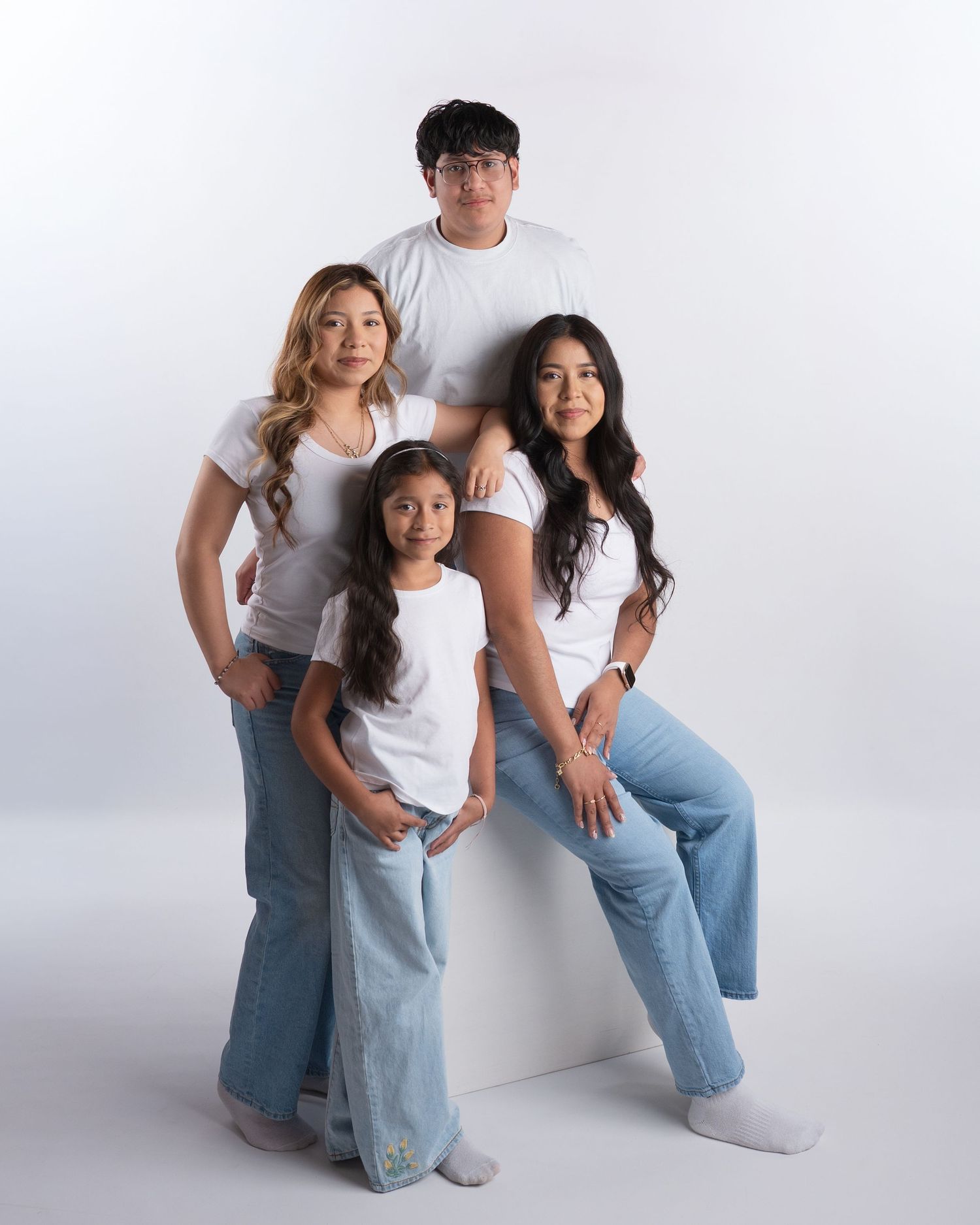 Family of four posing together in matching white shirts and jeans.