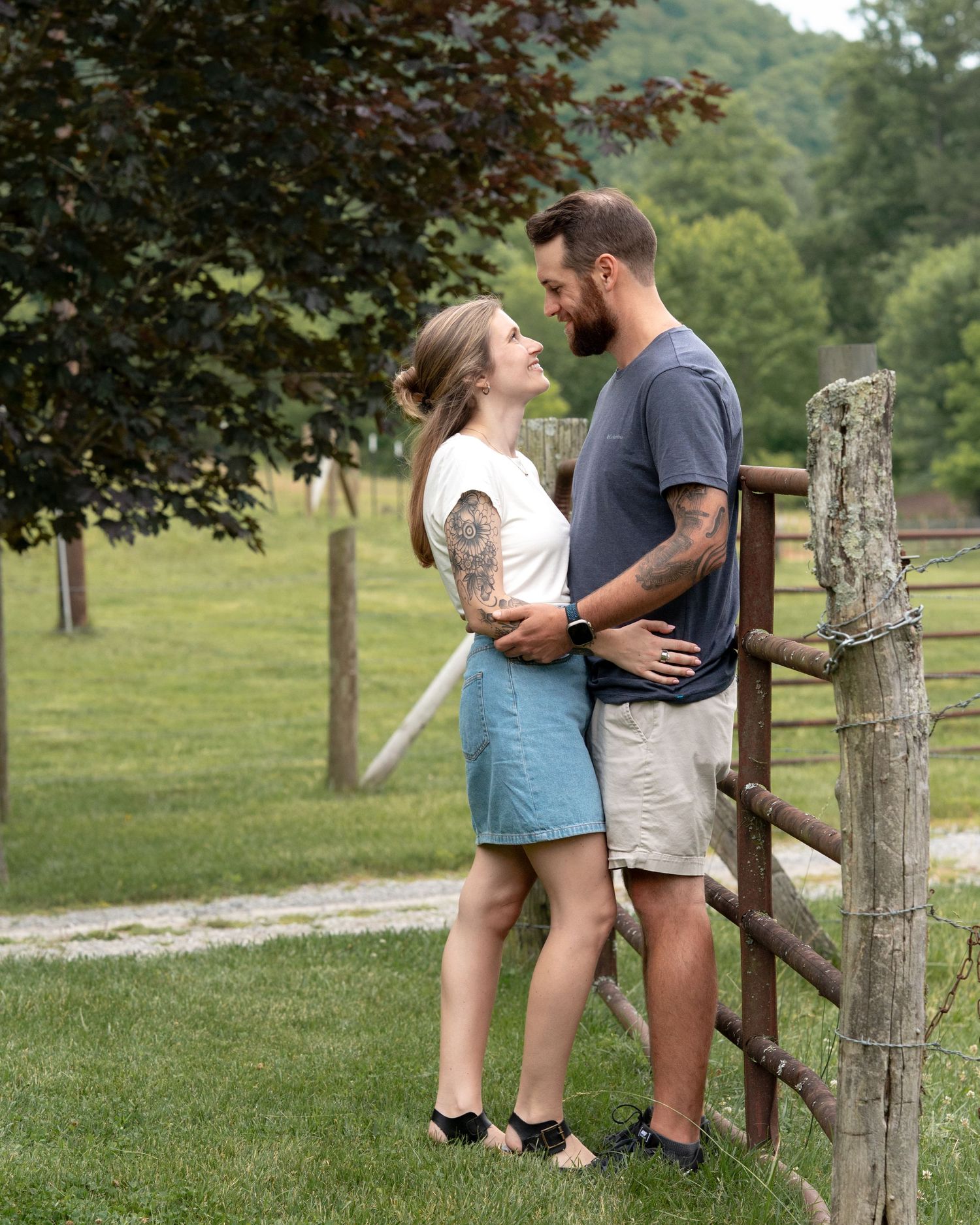 A loving couple shares a romantic moment gazing at each other beside a rustic wooden fence outdoors.