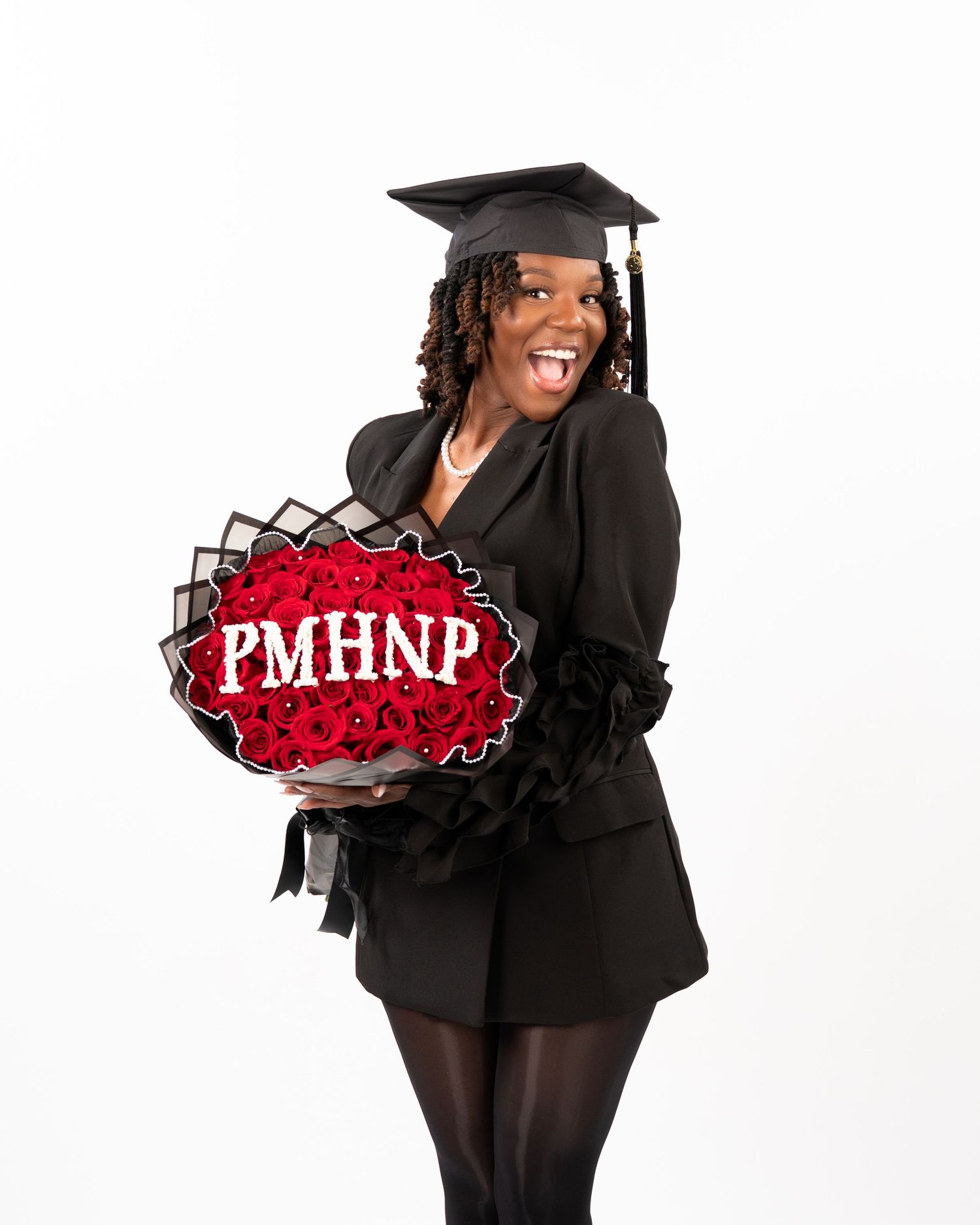 Excited graduate in black cap and gown holding bouquet of red roses with PMHNP sign.