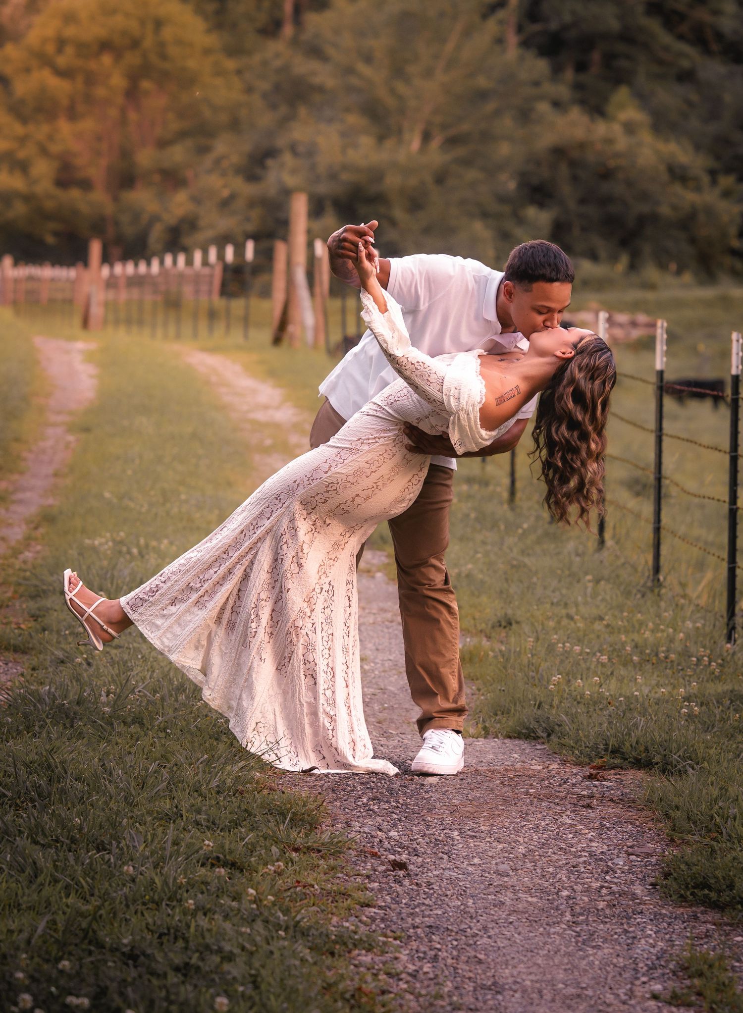Romantic couple sharing a dip kiss on a scenic outdoor pathway surrounded by lush greenery.