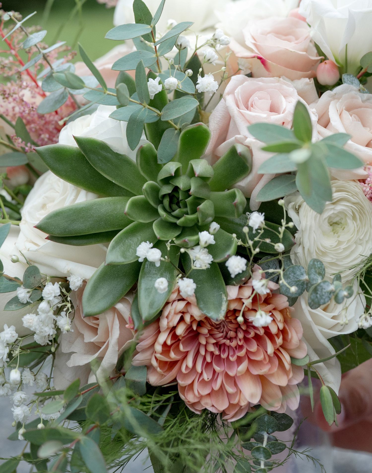 Elegant bridal bouquet with blush roses, succulents, ranunculus, coral mums, and baby's breath accented with eucalyptus greenery.