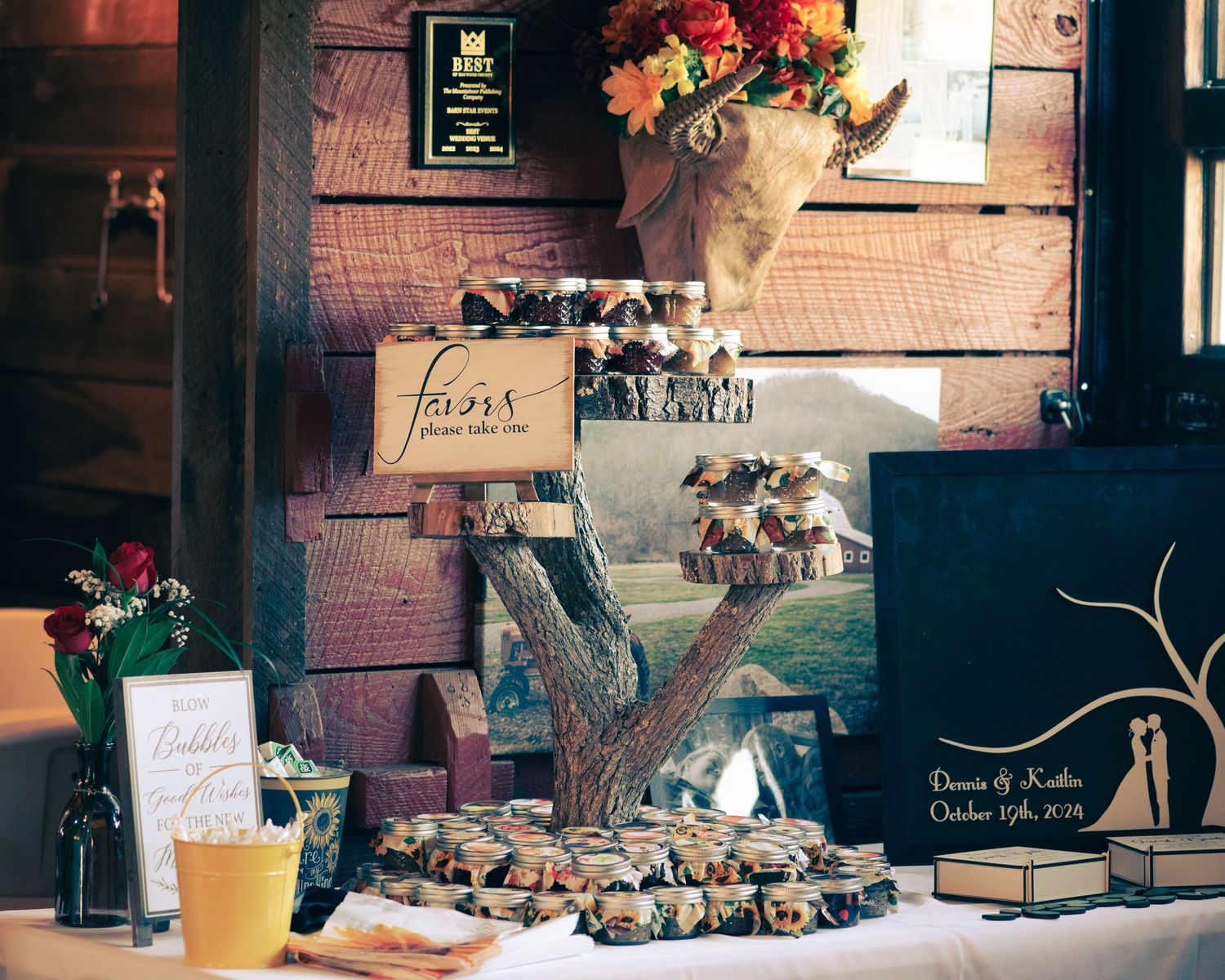 Rustic wedding reception table display with wooden signs, photos, and favors arranged on tree stump decor.