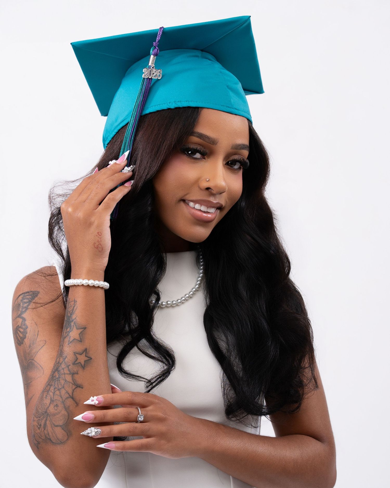 Graduate wearing teal mortarboard cap with tassel poses in white dress for a close-up portrait.