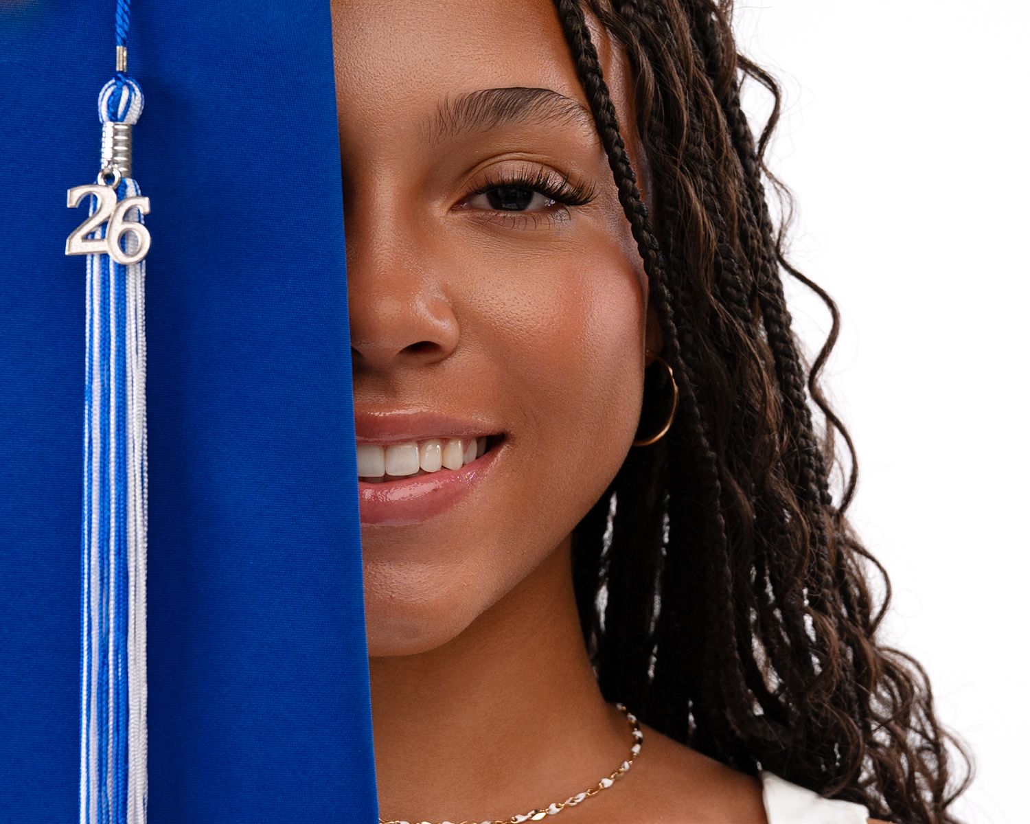 Close-up of smiling graduate wearing blue cap with class of 26 tassel for senior portrait.