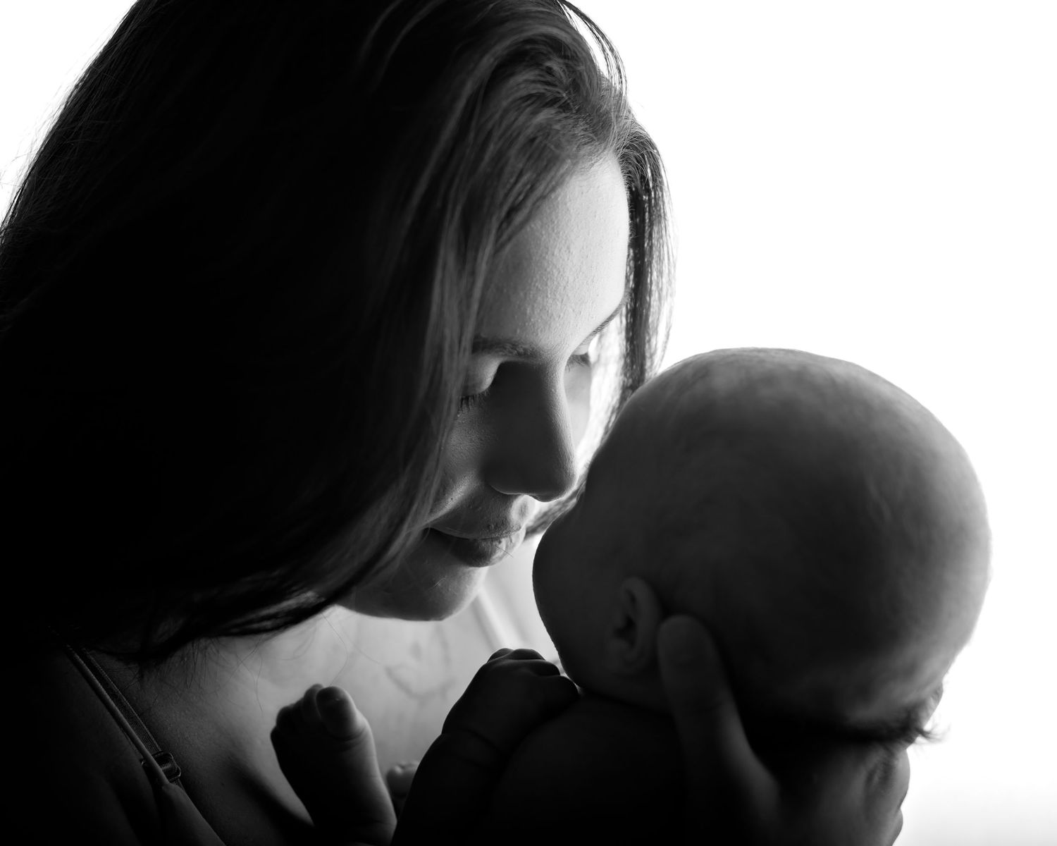 Black and white silhouette portrait of mother lovingly gazing at her newborn baby.