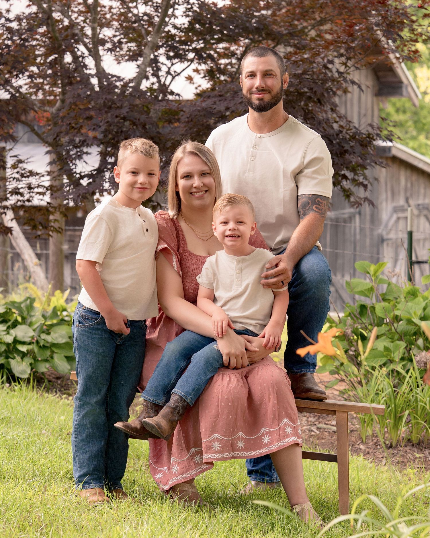 A happy family of four poses together on a garden bench surrounded by lush greenery.