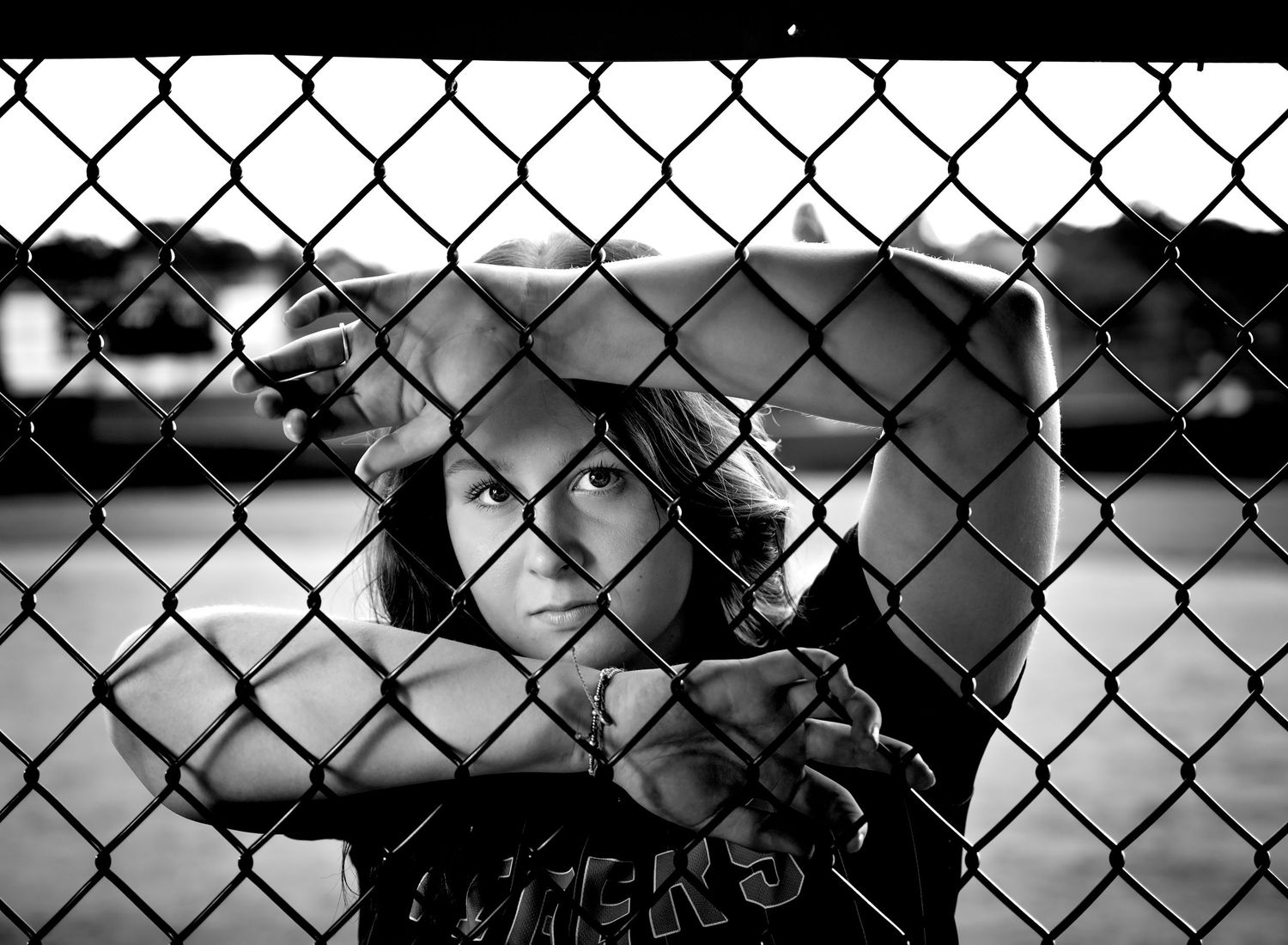 A young person grips a chain-link fence in a dramatic black and white portrait photo.