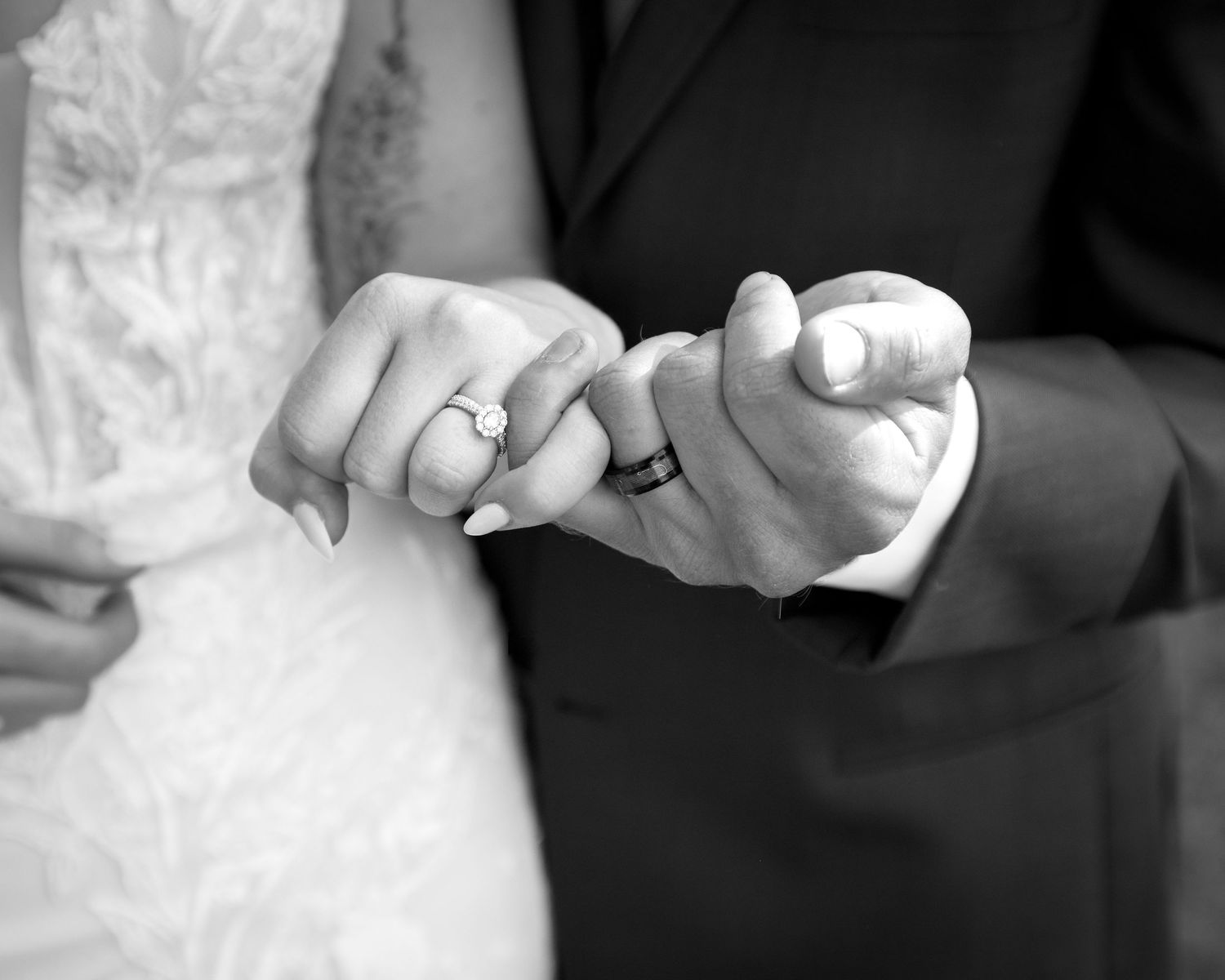 Black and white photo of bride and groom holding pinkies, showing wedding rings.