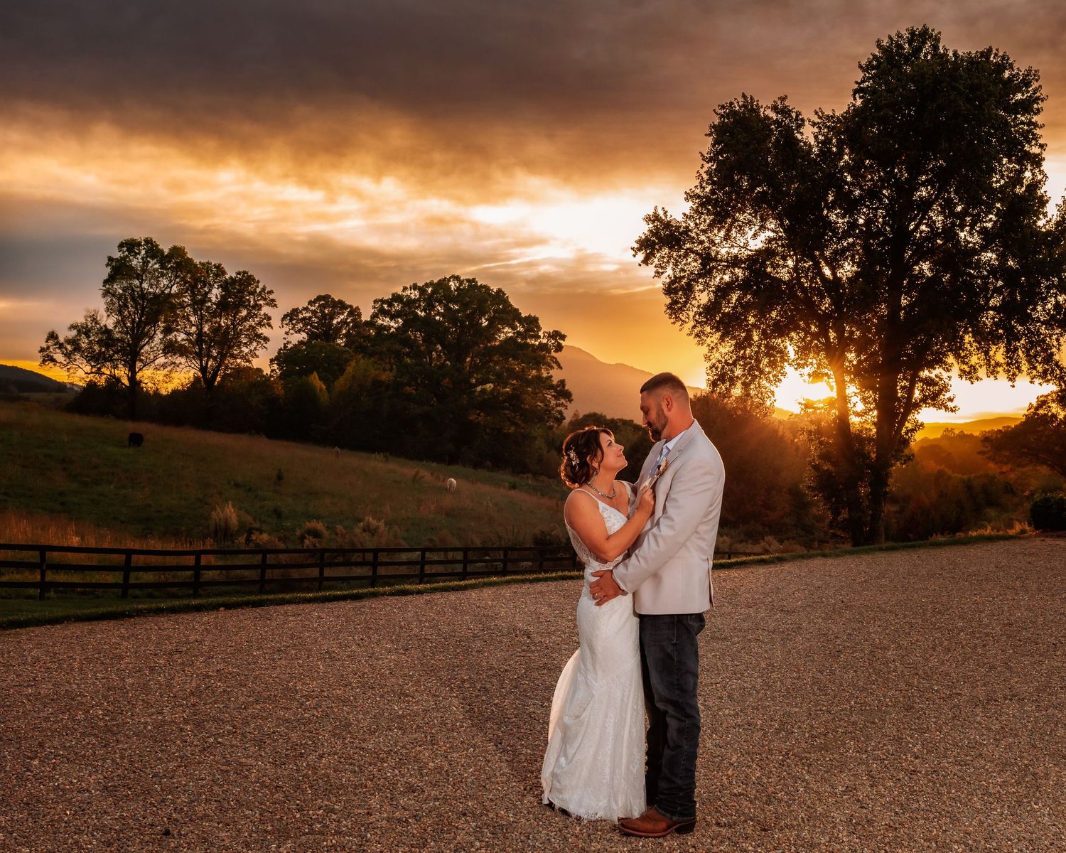 Bride and groom share a romantic embrace during a stunning golden sunset at an outdoor wedding venue.
