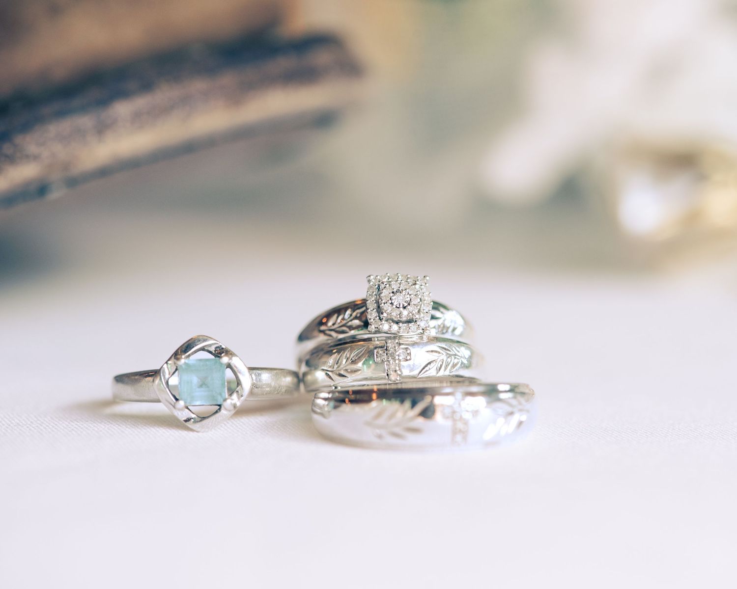 Three silver wedding rings arranged together, featuring a blue gemstone, diamond halo, and engraved band.