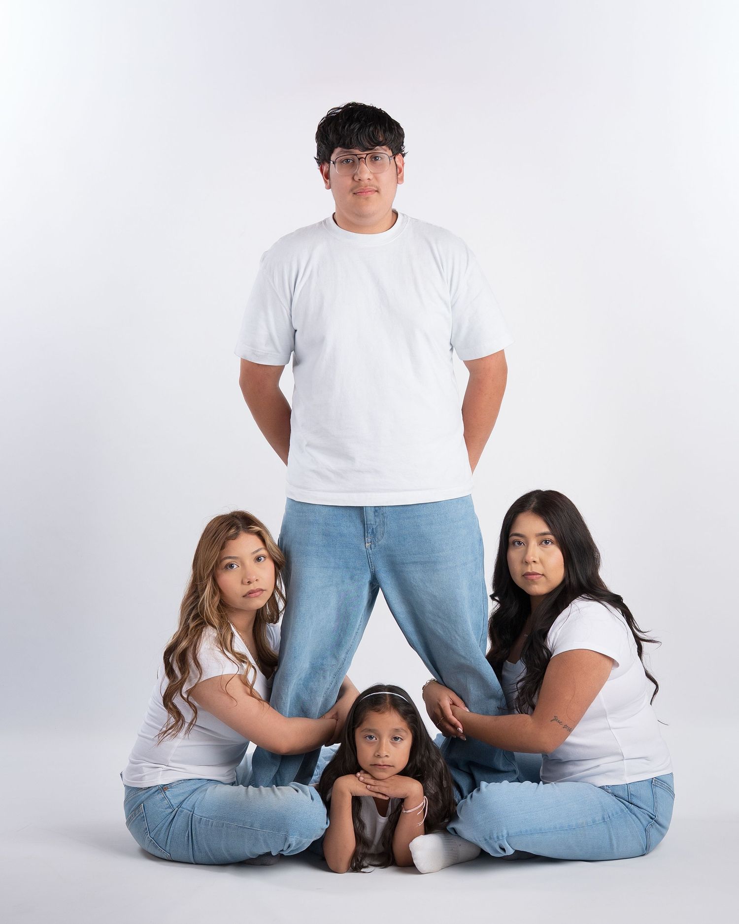 Four siblings in white tees and jeans pose in a creative stacked formation in a studio.