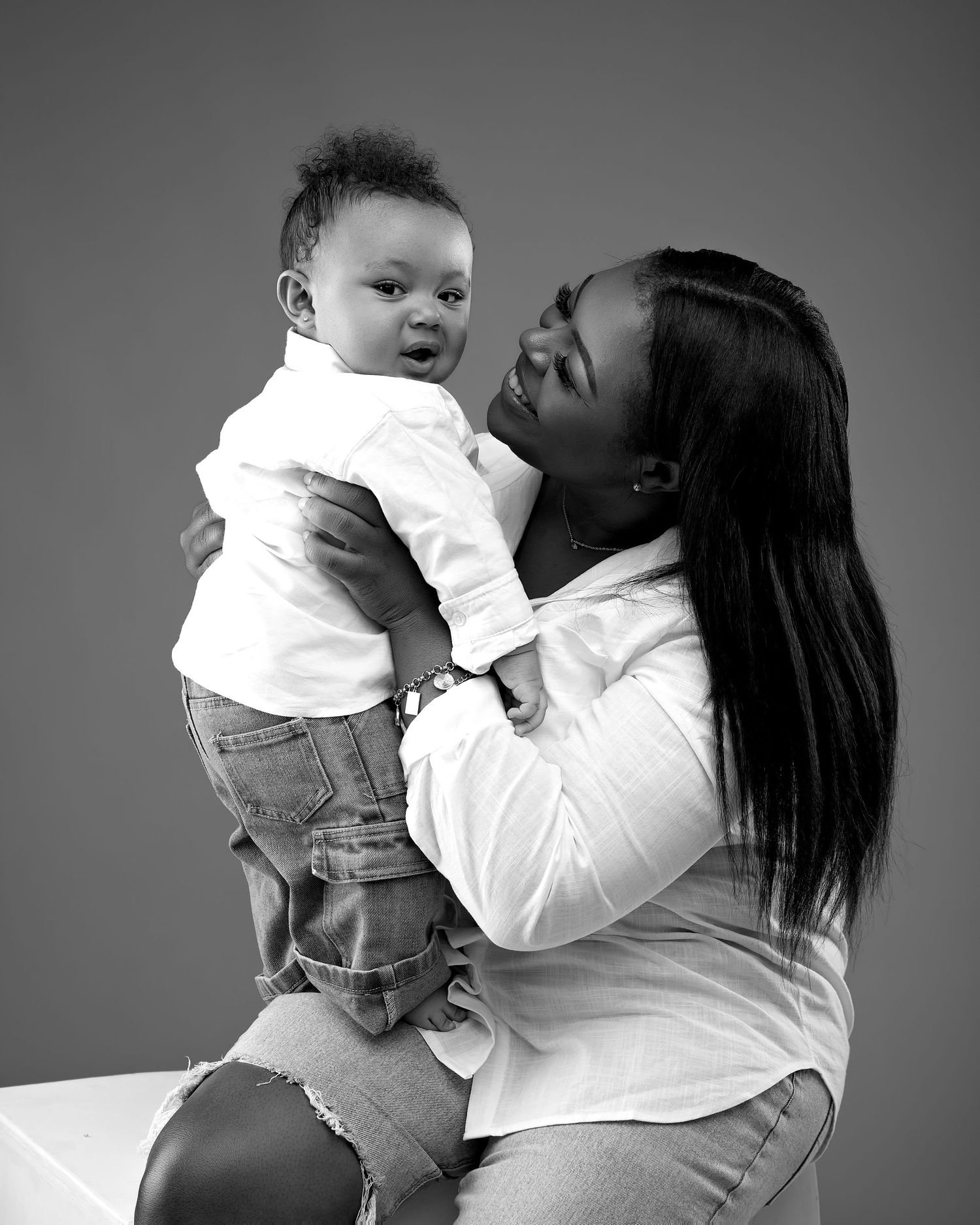 Black and white photo of mother lovingly holding infant baby during professional portrait session.