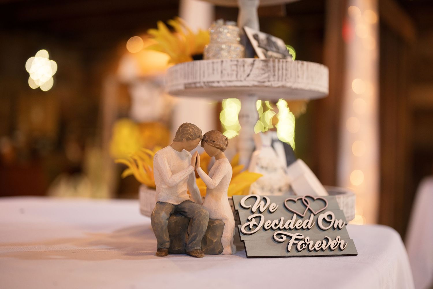 Wedding cake topper figurines beside a sign reading We Decided On Forever at a rustic barn reception.