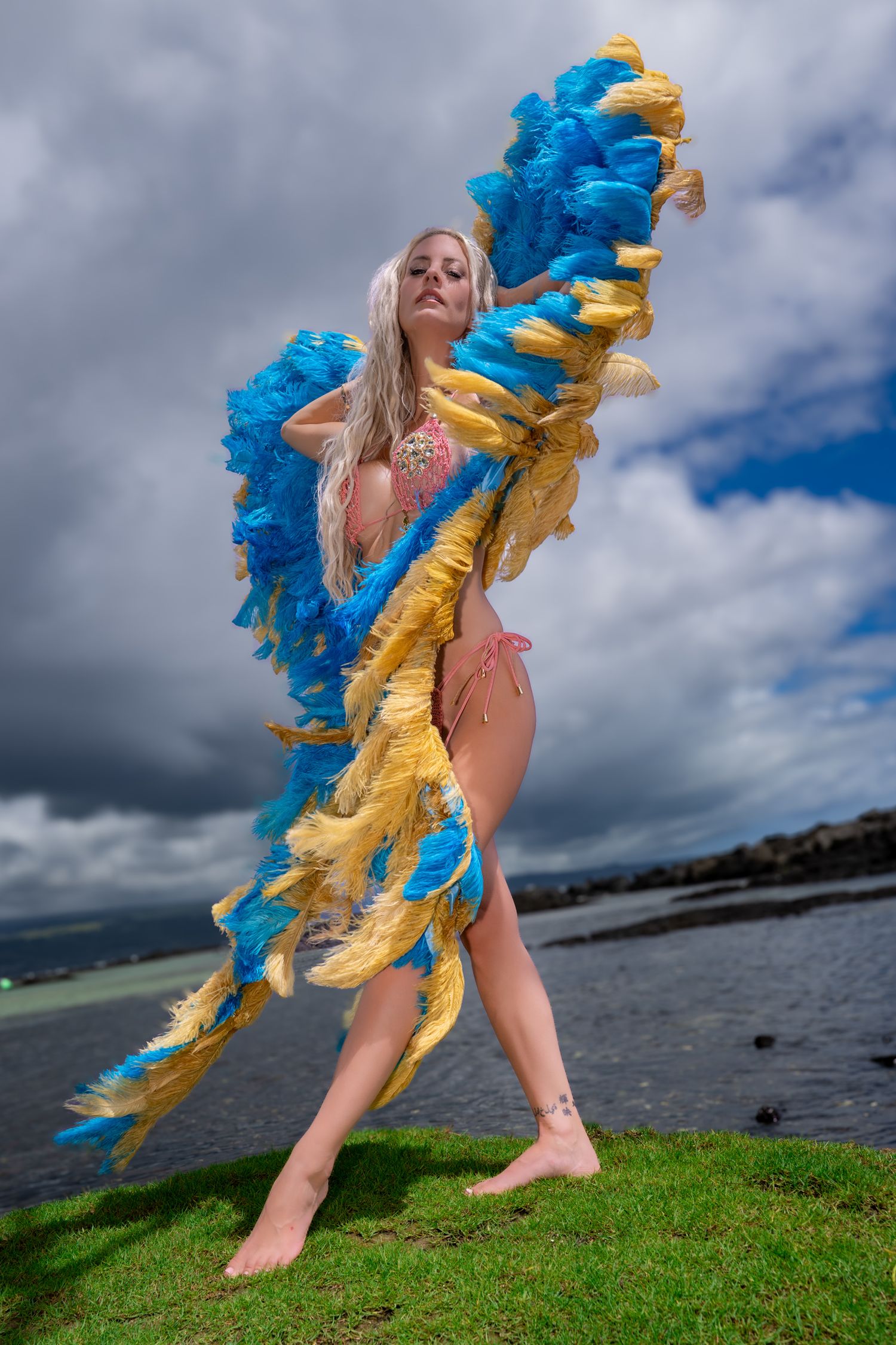 Siren Couture fashion portrait with blue and gold feathered wings beside the water in Hawaii.
