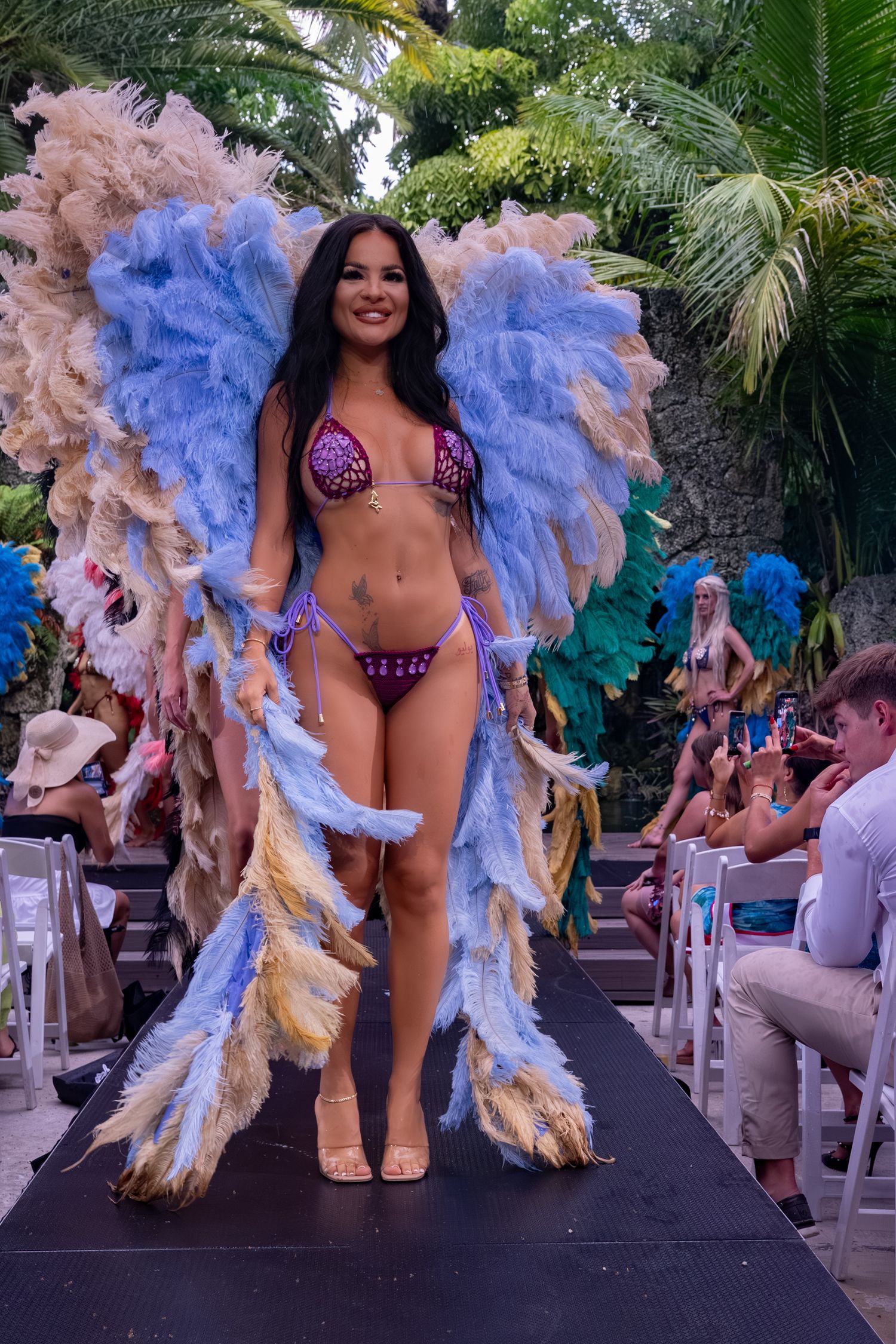 Siren Couture model wearing lavender feathered wings on an outdoor runway in Miami.