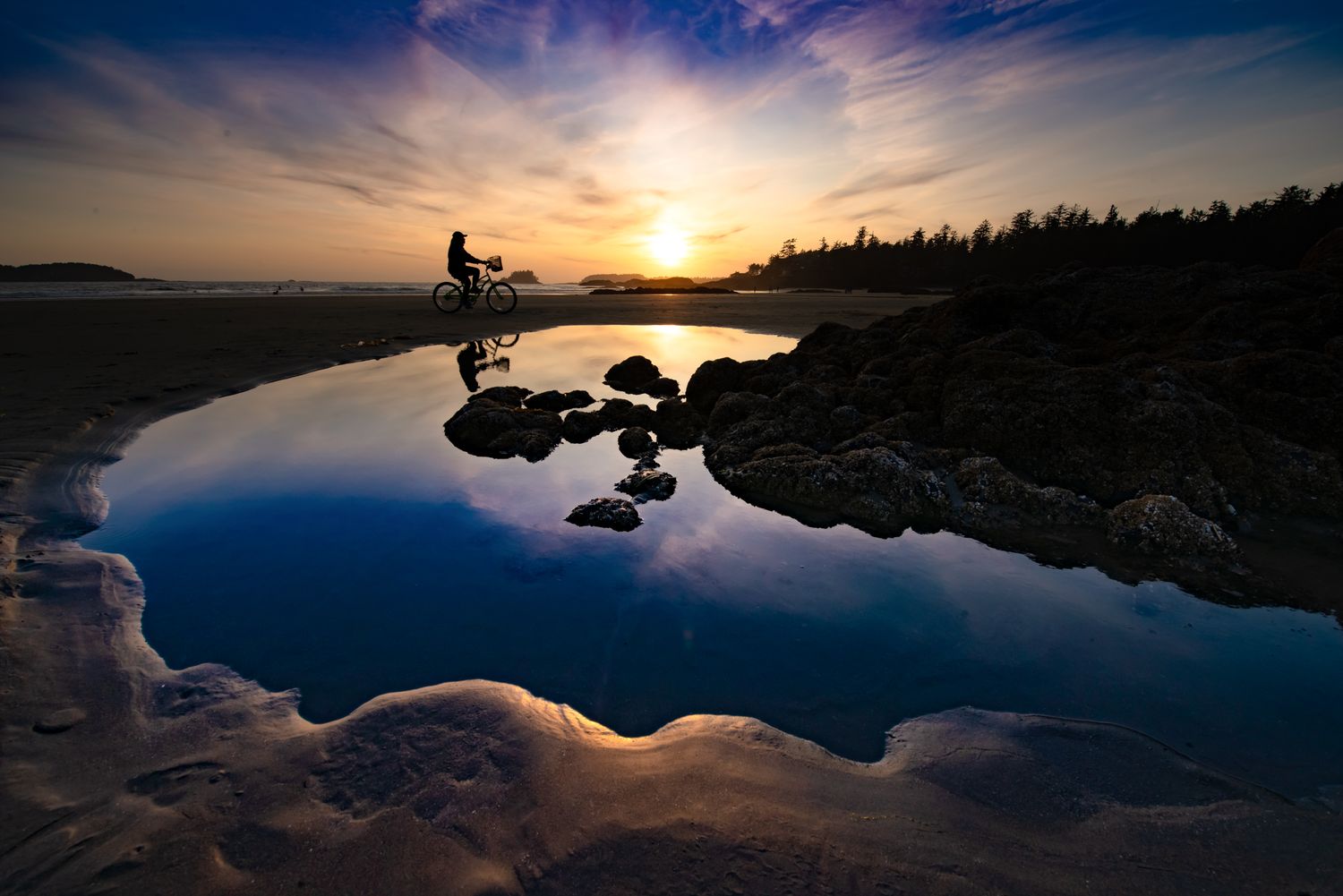 Cyclist riding along a reflective Tofino beach beneath a glowing sunset sky.