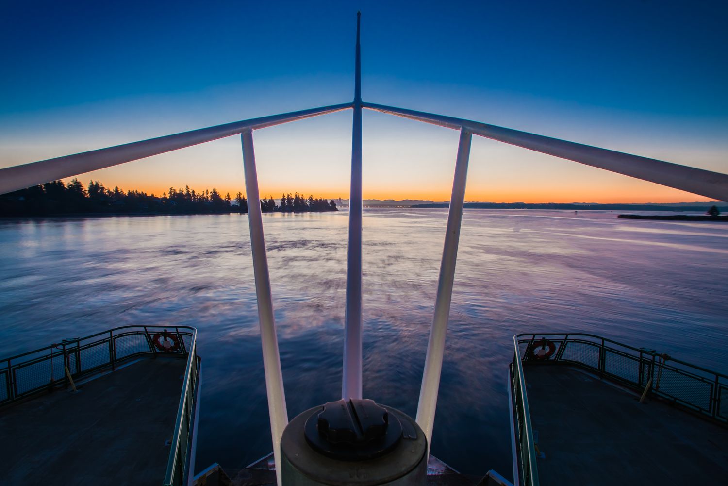 View from a ferry bow across calm water beneath a blue and gold dawn sky.