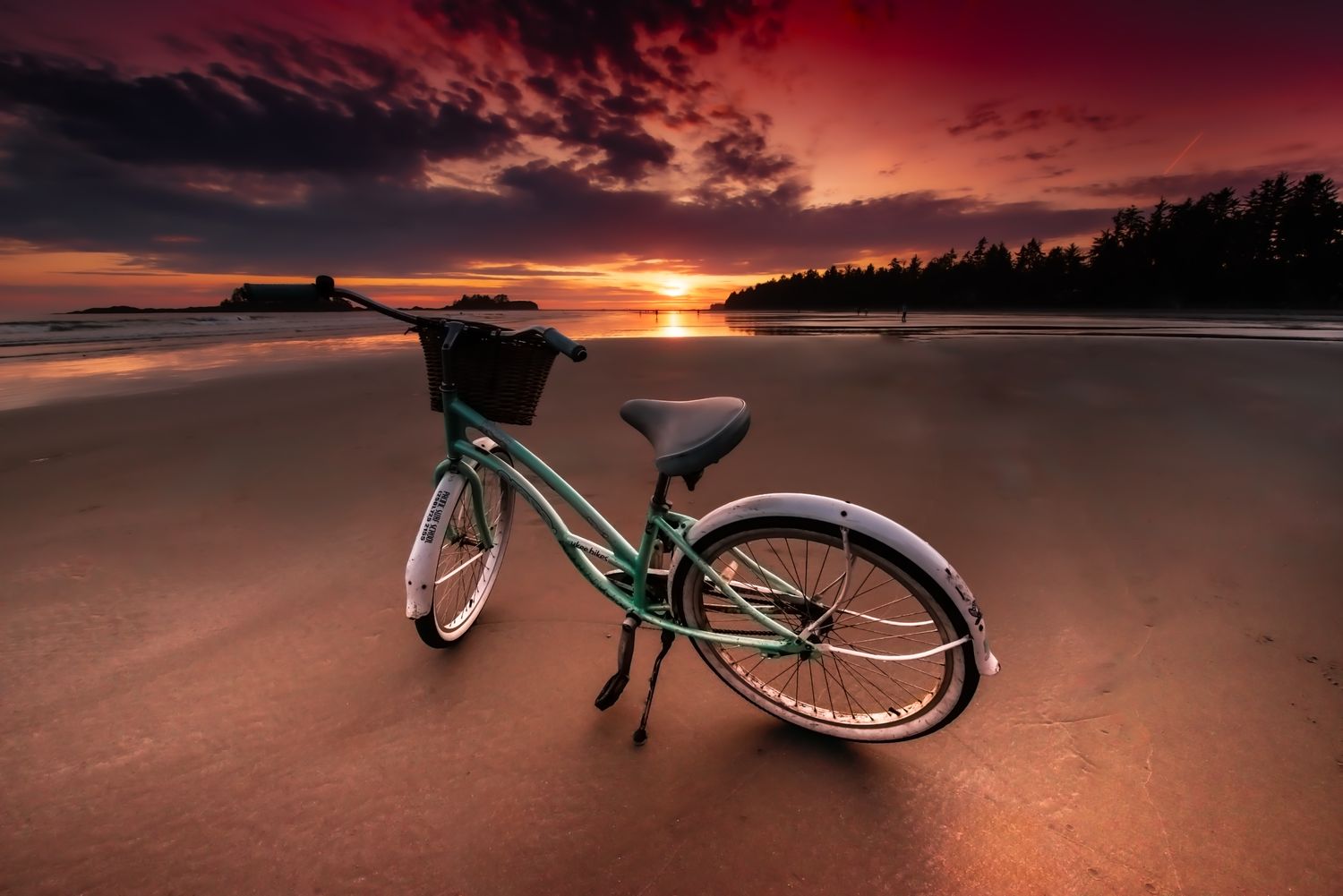 A mint-green bicycle on the wet sands of Tofino beneath a vivid sunset.