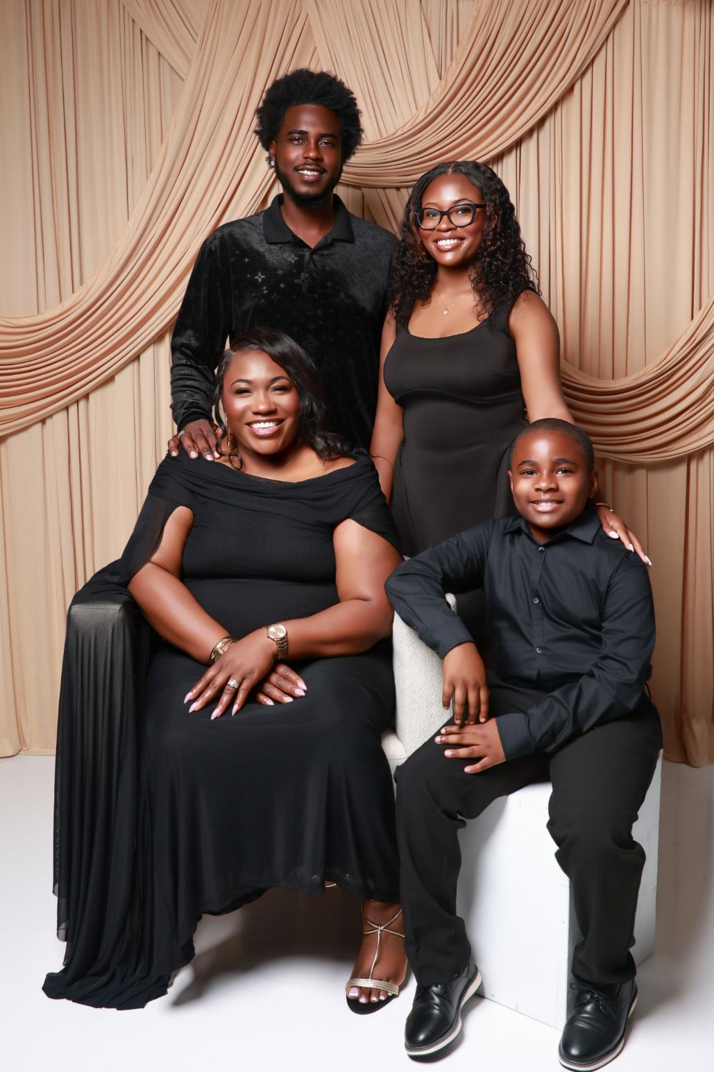 A family of four dressed in elegant all-black outfits poses for a professional studio portrait.