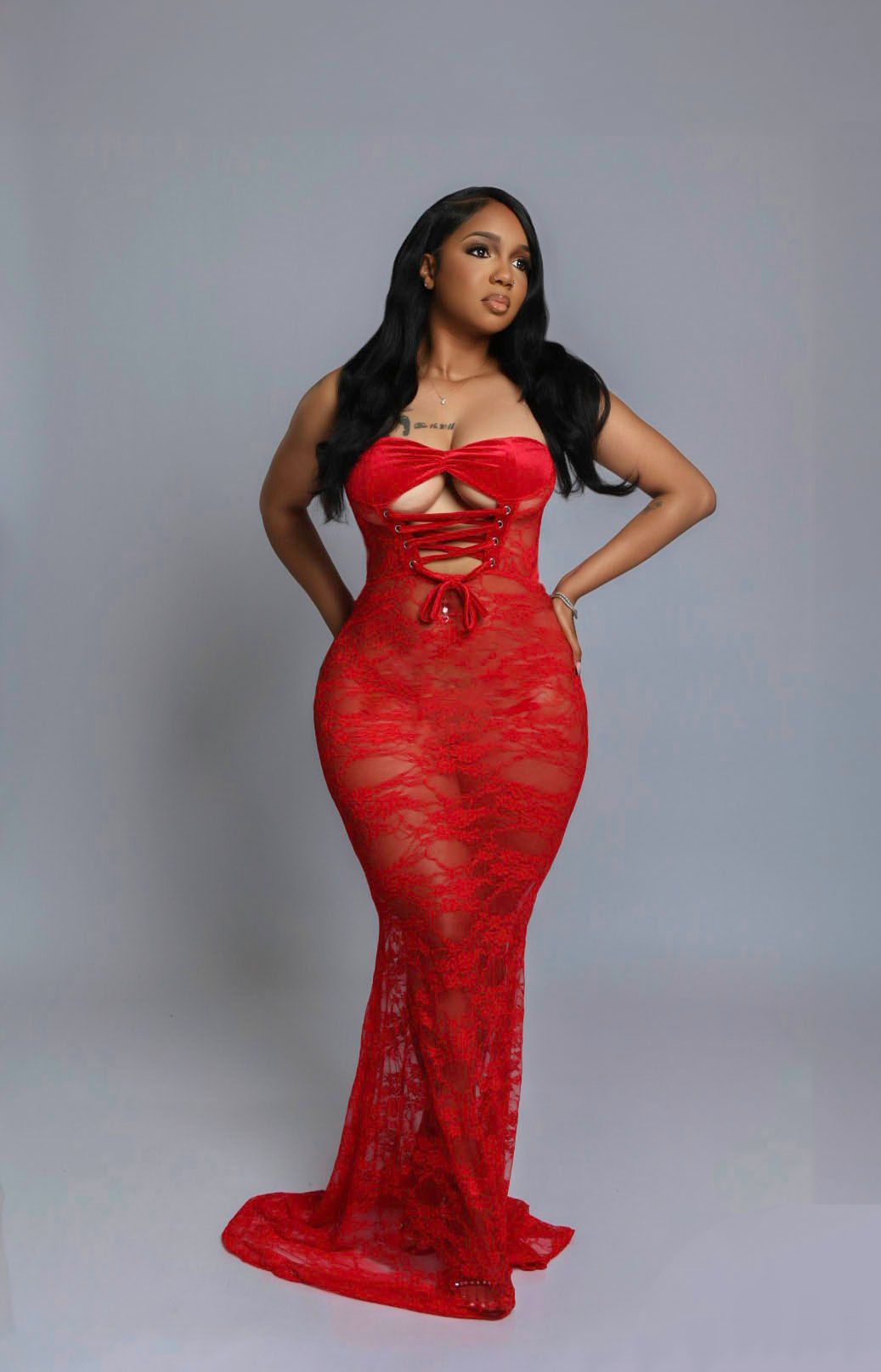 Woman in a red lace form-fitting gown posing against a neutral gray background.