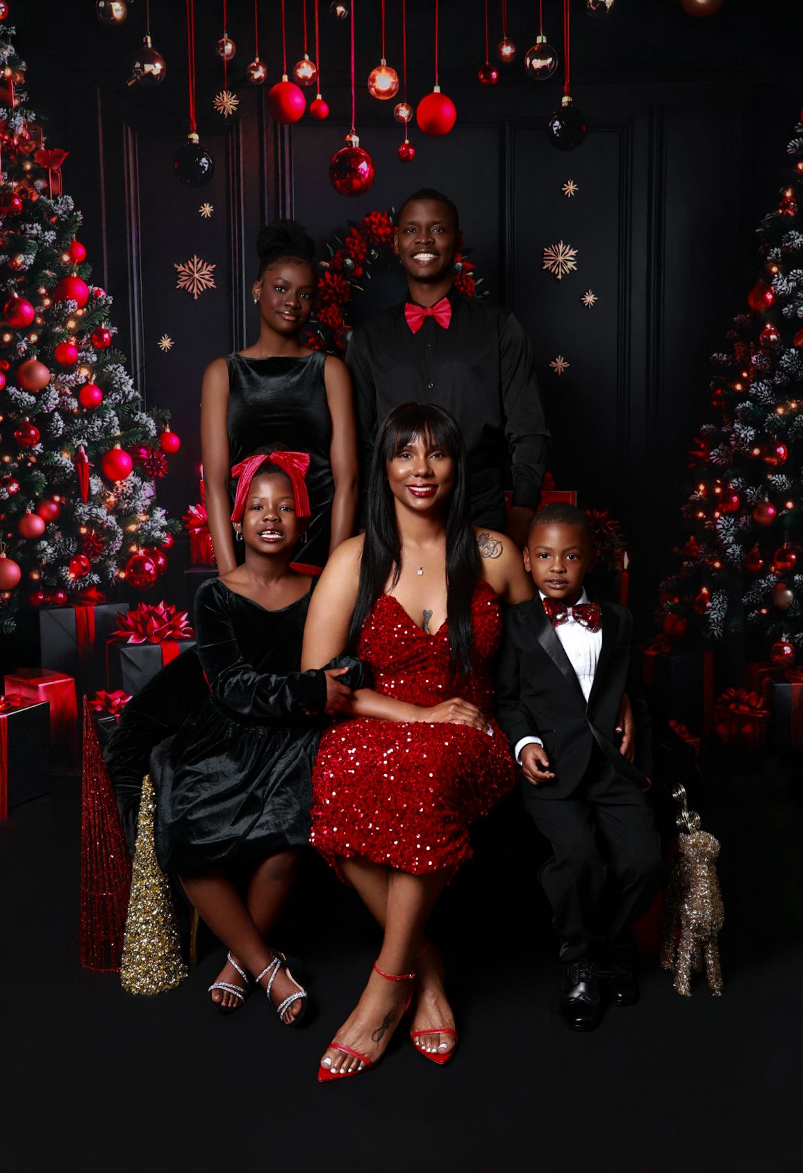 Family of five in elegant red and black attire posing before Christmas trees.