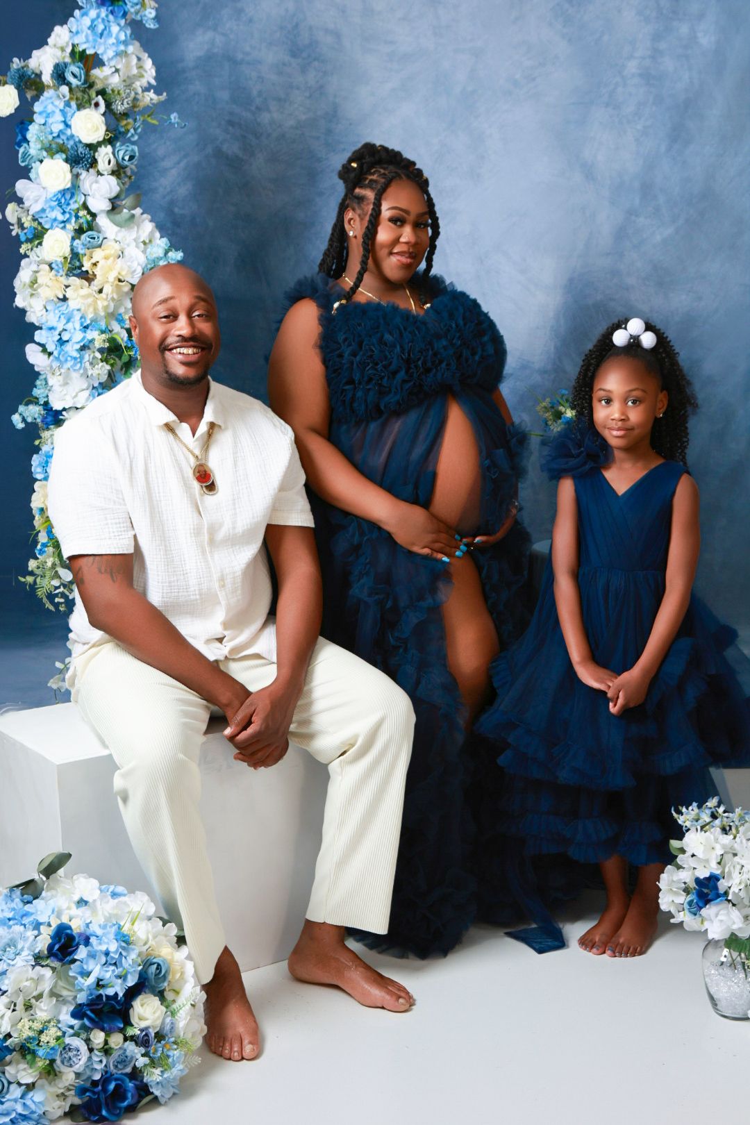 Family maternity photo shoot with parents in navy blue and white outfits with young daughter in blue dress.