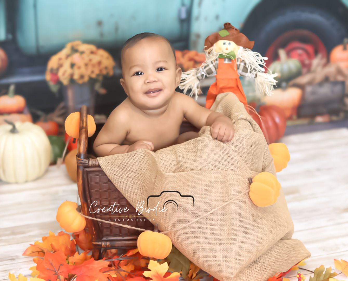 Cheerful baby sits in rustic wooden crate with autumn pumpkin farm themed photography backdrop.