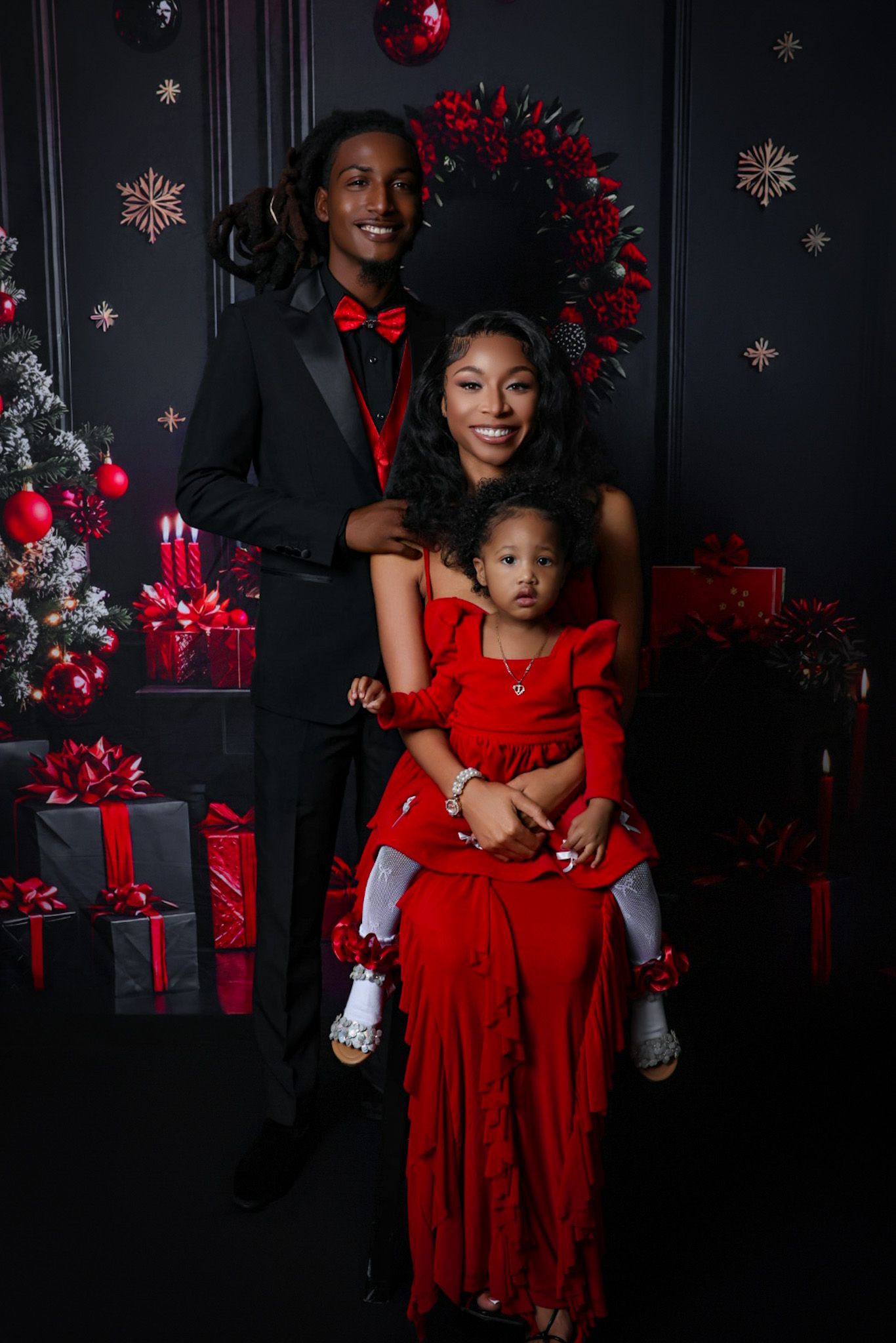 Young family in red and black holiday outfits posing before Christmas decorations.