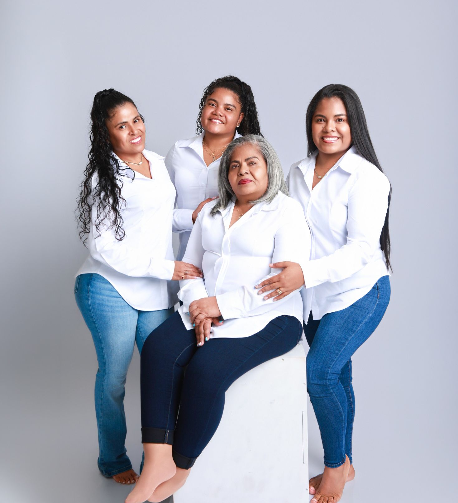 Four women in matching white shirts and jeans pose together in a warm family portrait studio photo.