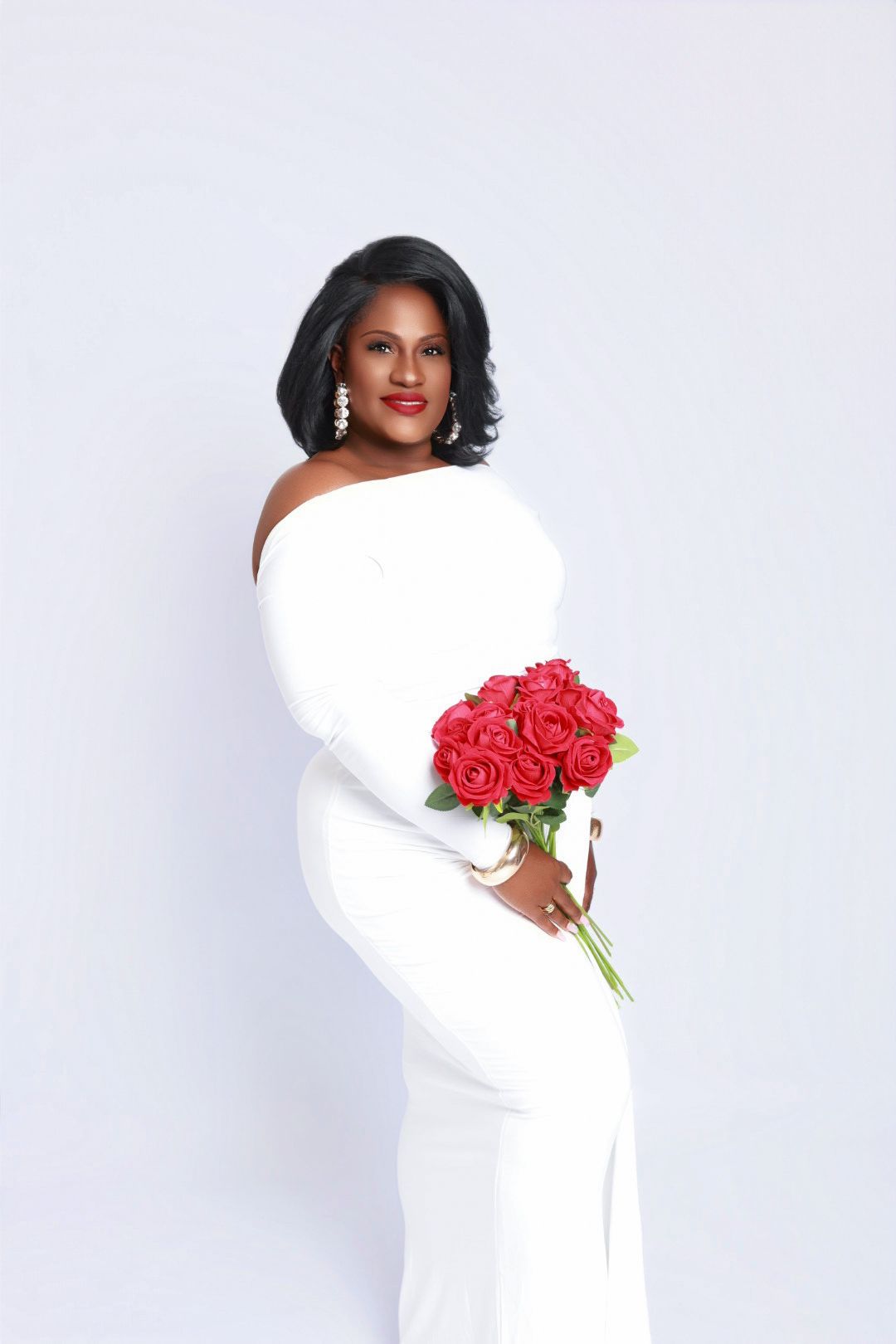 Woman in white off-shoulder gown holding red roses bouquet in an elegant studio portrait.