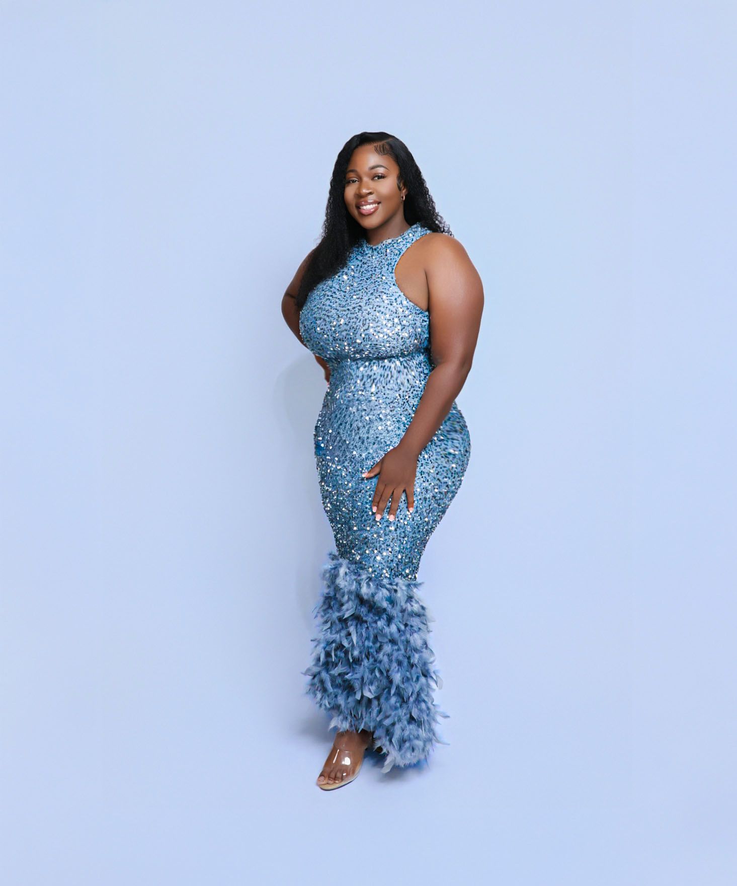Woman in blue sequin feather mermaid gown poses against light blue studio background.