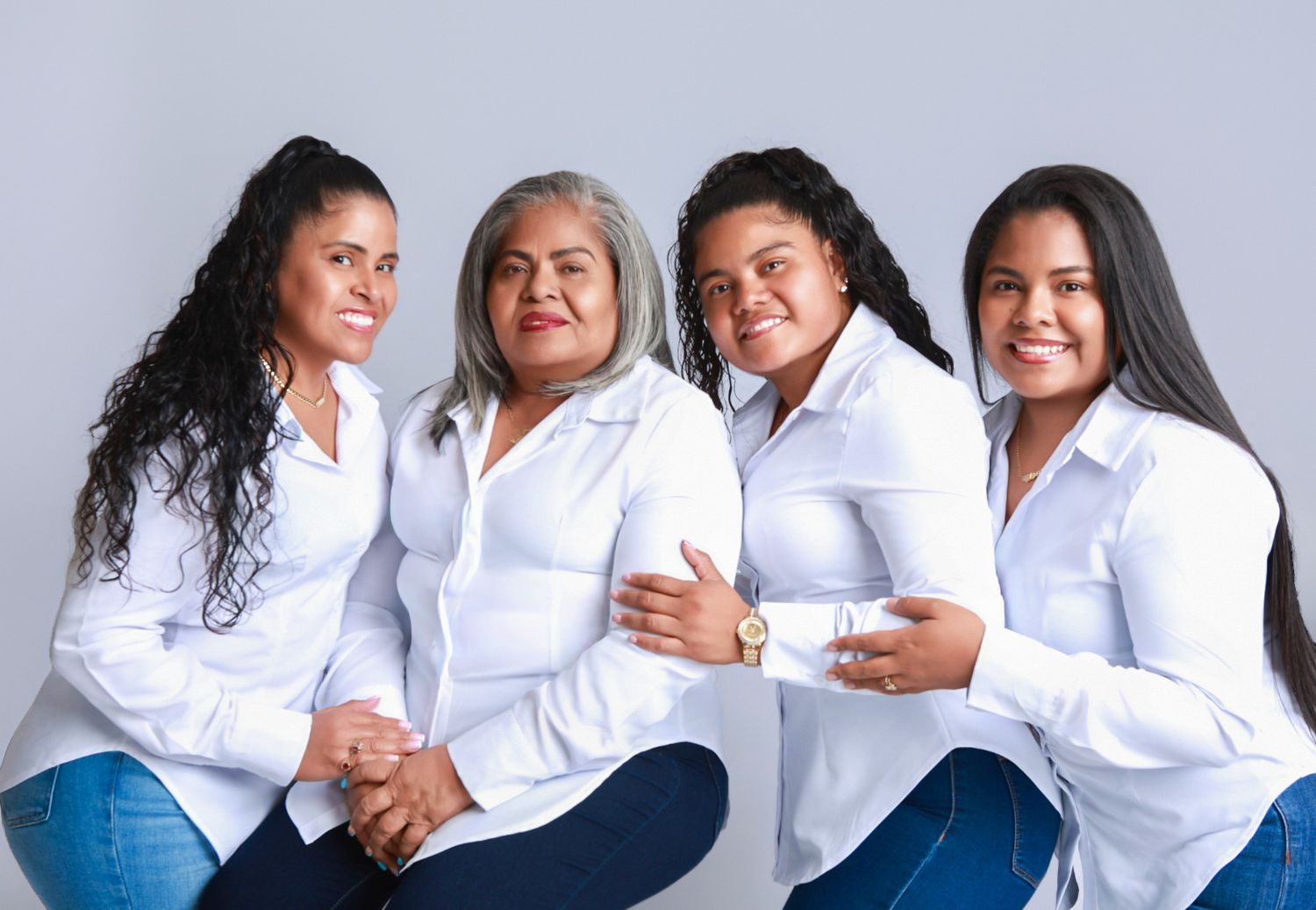 Four women in white shirts and jeans sit together smiling in a casual family studio portrait.