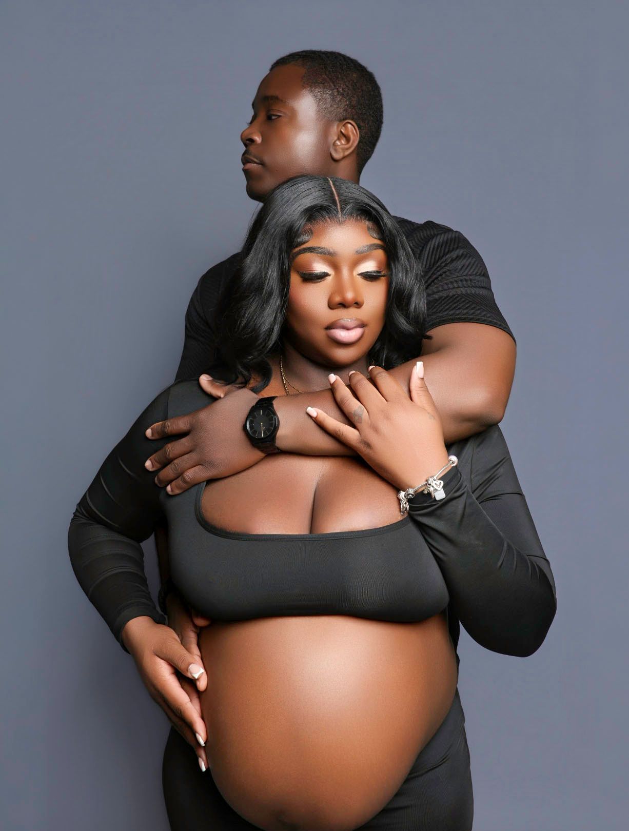 Intimate couple maternity photo shoot with both wearing black outfits on gray background.